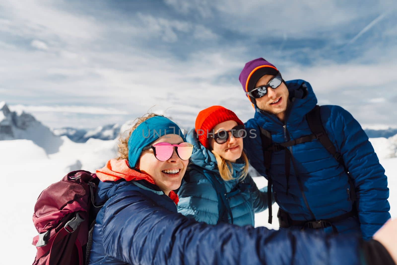 Smiling group of three mountaineers taking a selfie up in the sunny snowy mountains by VisualProductions