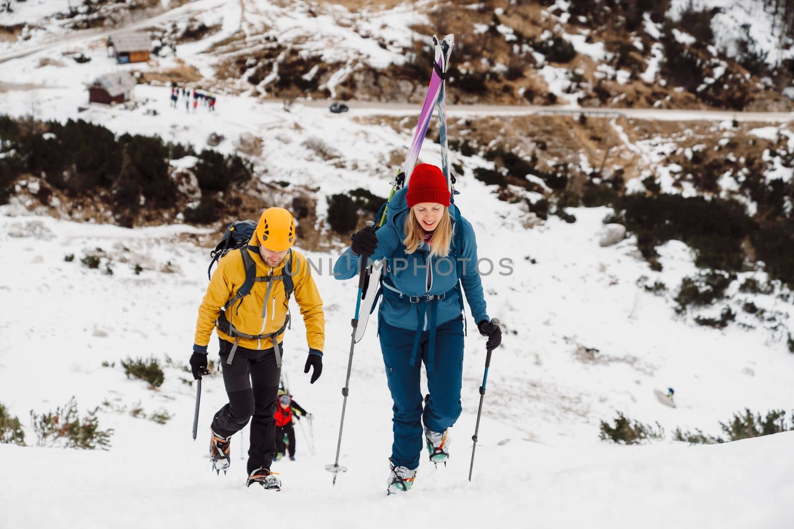 Couple of mountaineers climbing up a snowy mountain, woman carrying skis on her back by VisualProductions