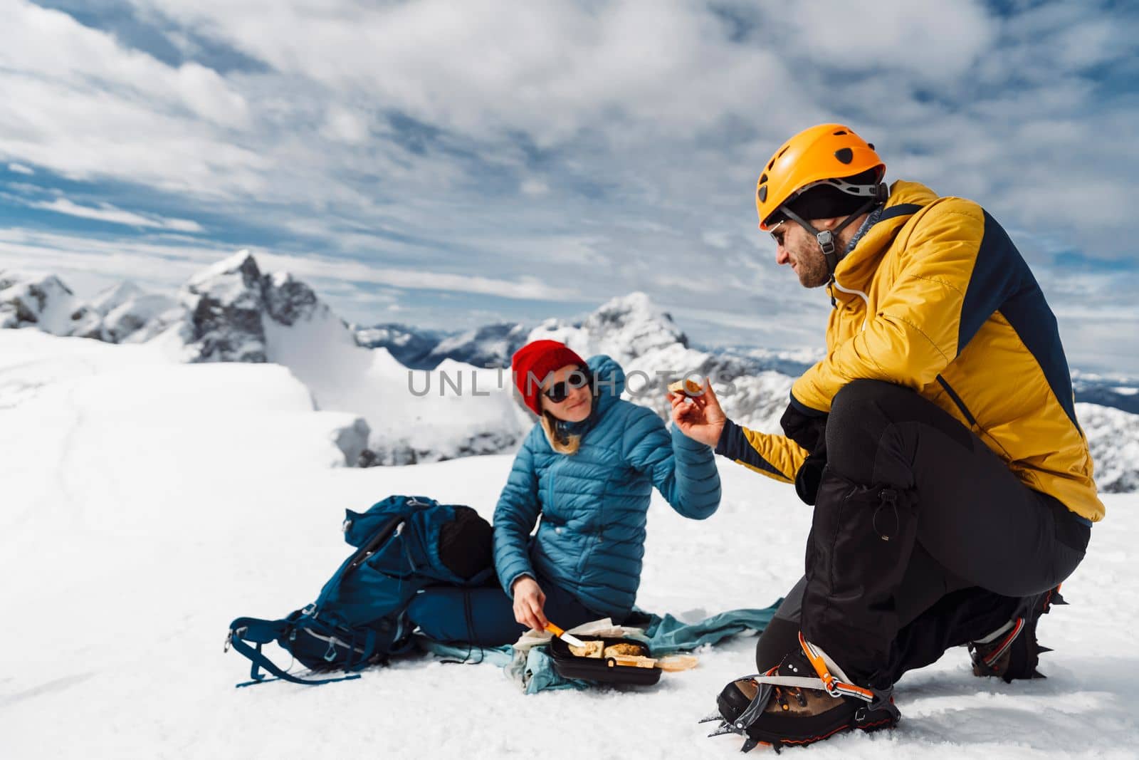 Mountaineering couple having lunch on top of the snowy mountain, sitting on the sun in the snow by VisualProductions