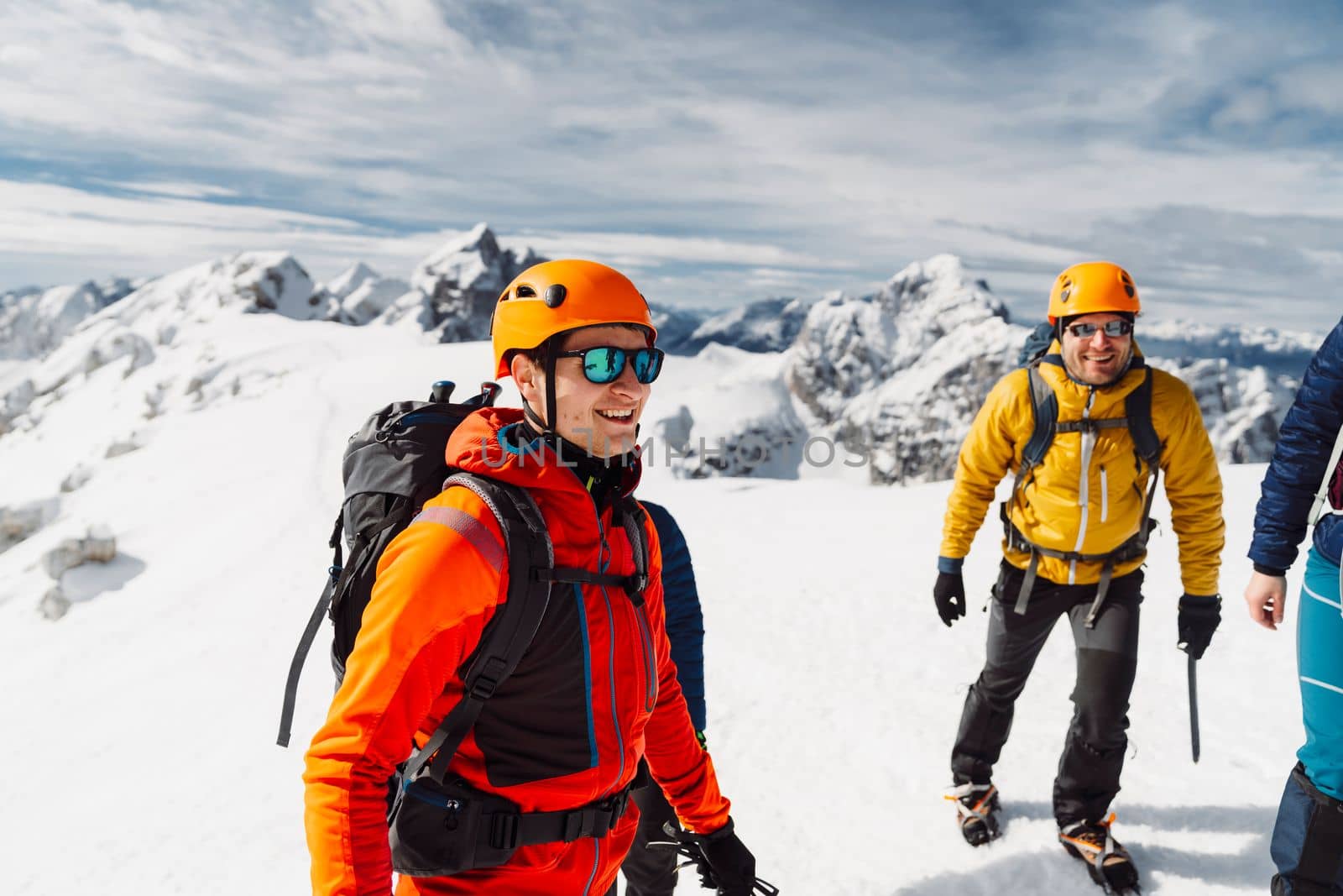 Mountaineer in orange jacket and protective helmet talking to the group while they enjoy the sun on top of the mountain by VisualProductions