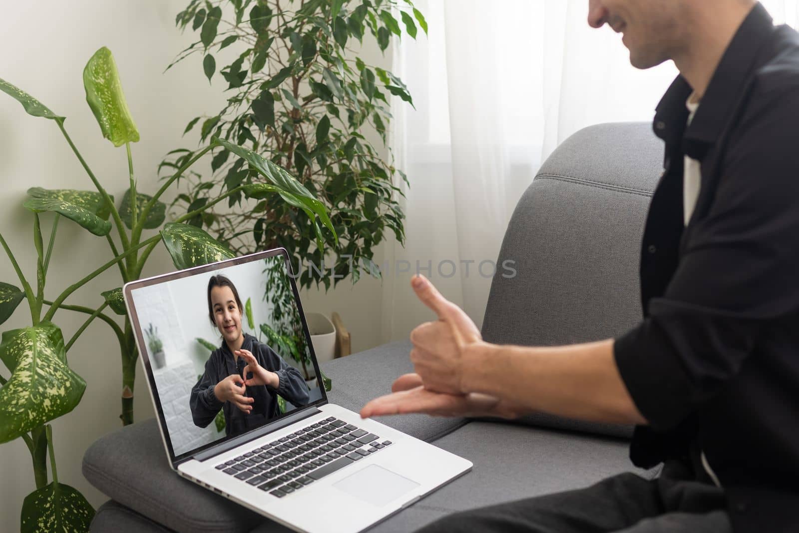 Happy smiling deaf young caucasian man uses sign language while video call using laptop while sitting at home, virtual communication concept