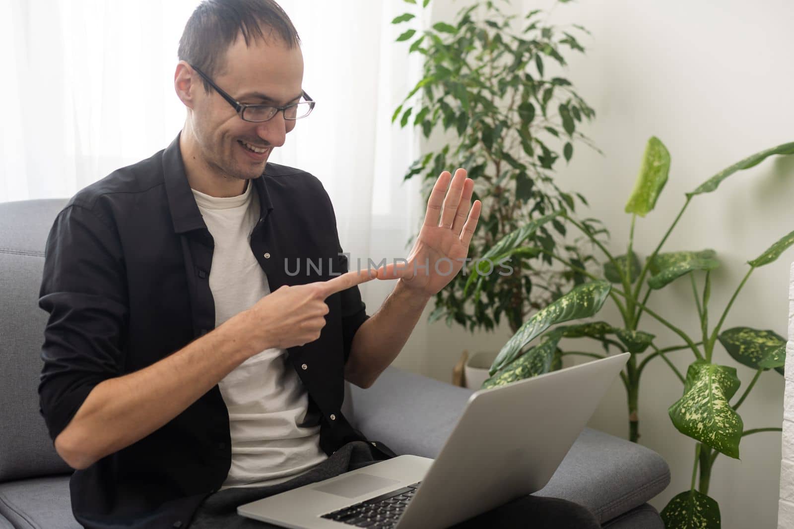 Happy smiling deaf young caucasian man uses sign language while video call using laptop while sitting at home, virtual communication concept
