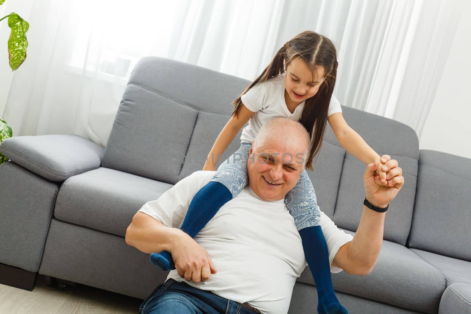Cute little girl spending time with positive active grandpa in living room by Andelov13