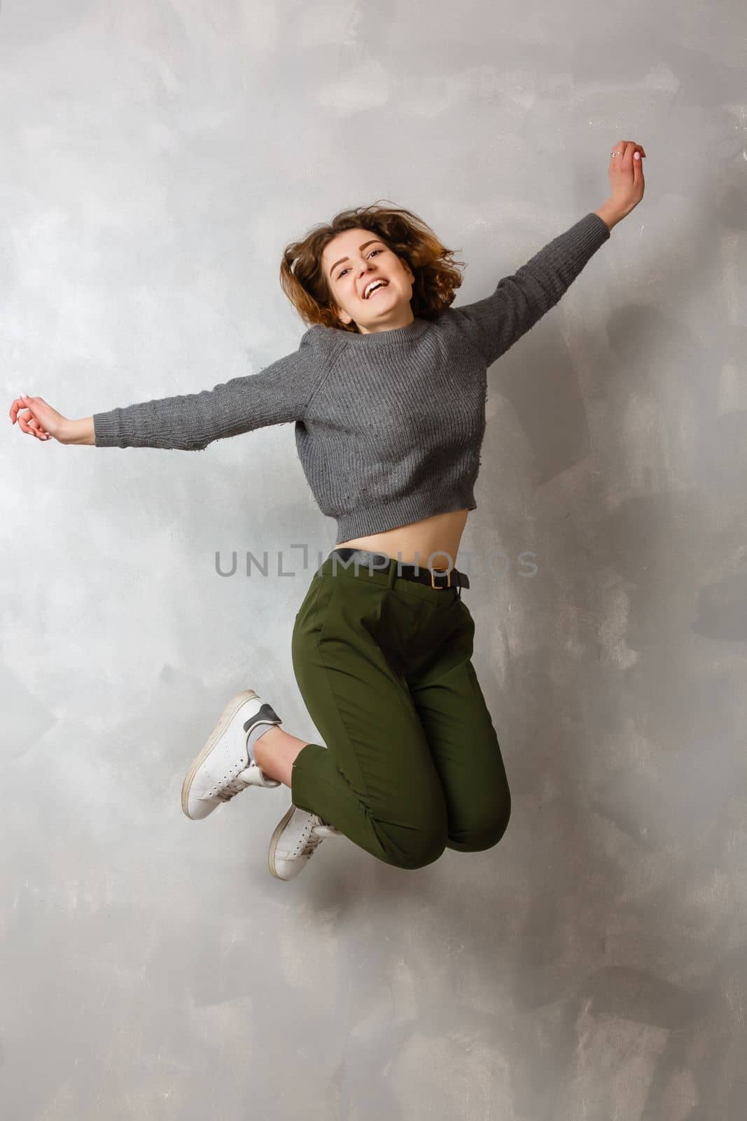 Full length portrait of a cheerful casual asian woman jumping isolated over gray background by Andelov13