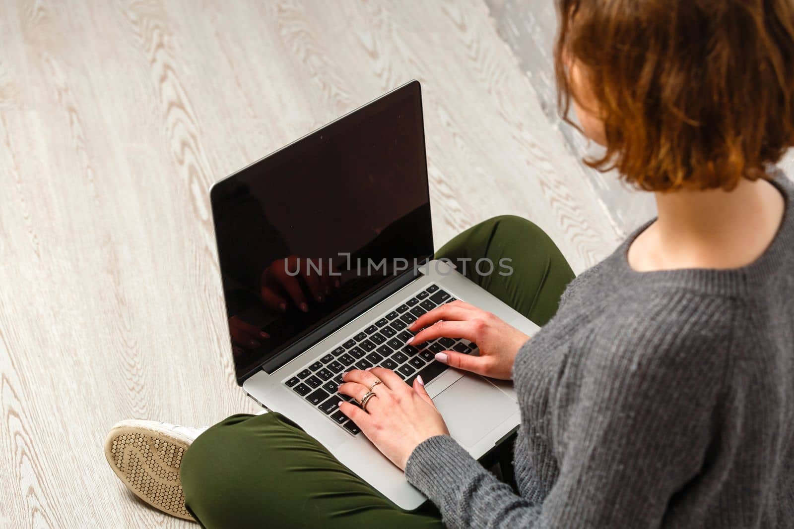 Happy young woman sitting on the floor with crossed legs and using laptop on gray background by Andelov13