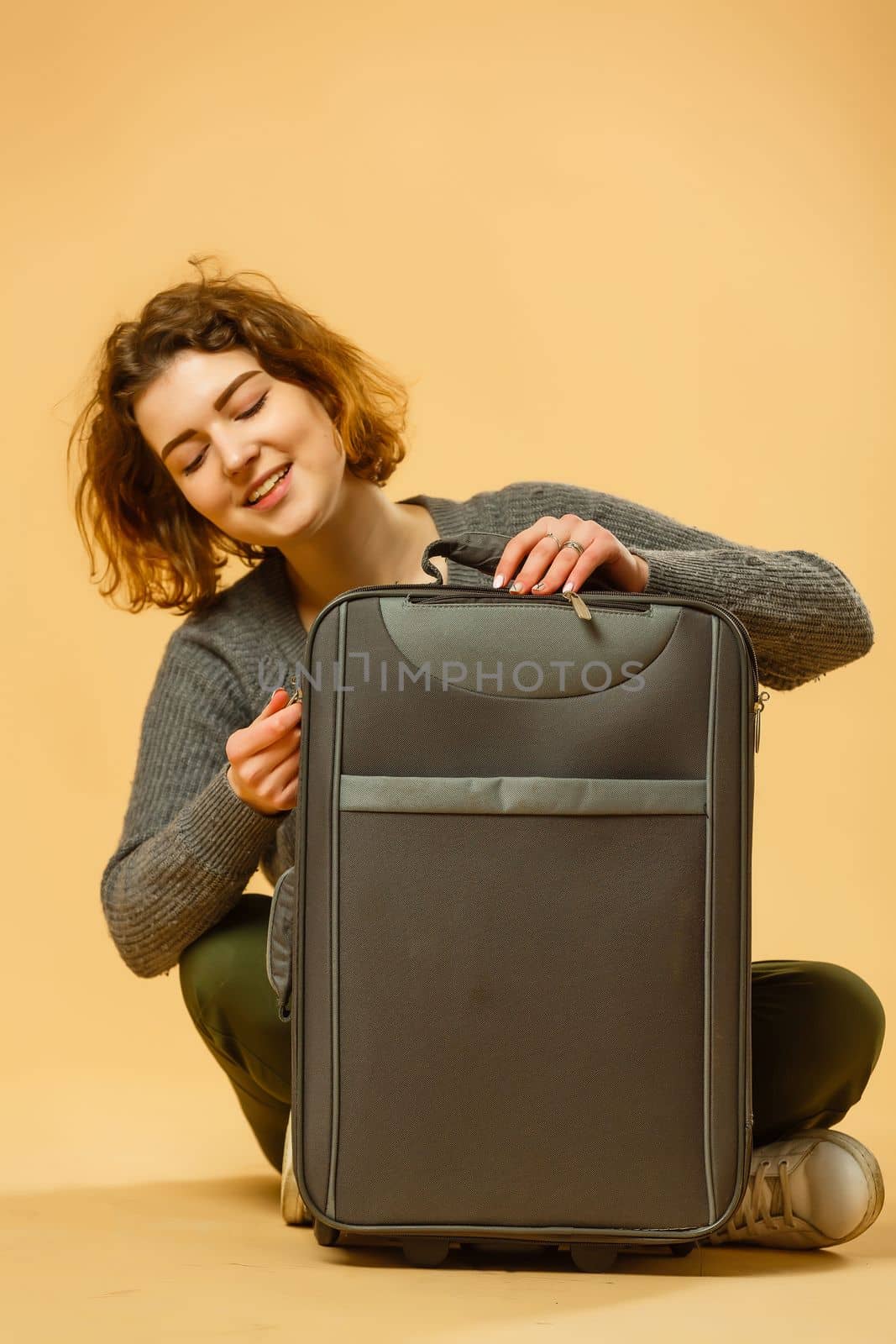 Ready for vacation. Traveling concept. Young excited woman sitting luggage valise. Isolated