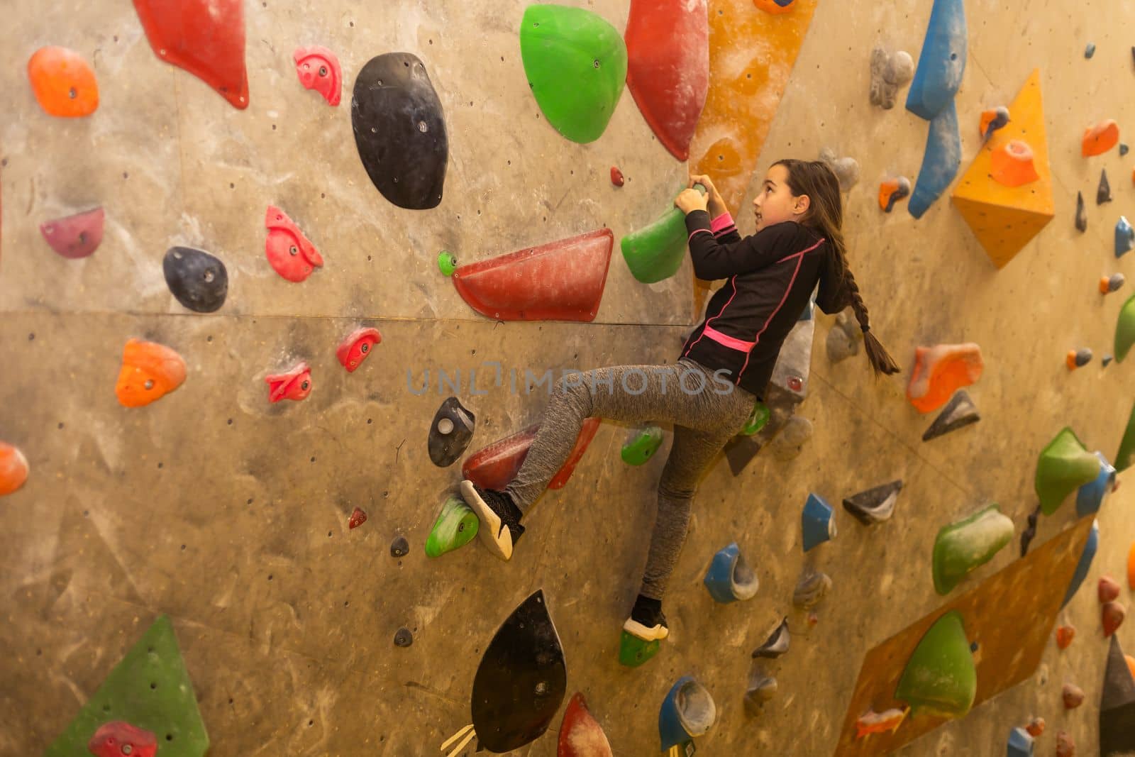 Teenage girl at indoor climbing wall. Kid having fun at bouldering wall. Child learning at climbing class. Sports healthy lifestyle. Youth at climbing summer camp by Andelov13