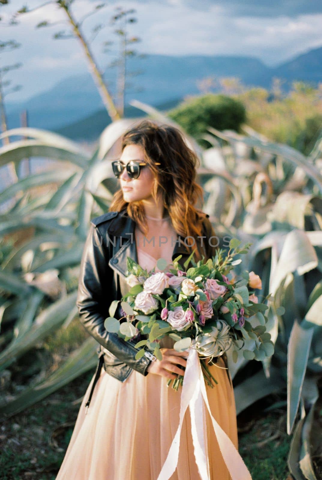 Bride in sunglasses with a bouquet of flowers stands near the agave bush. High quality photo