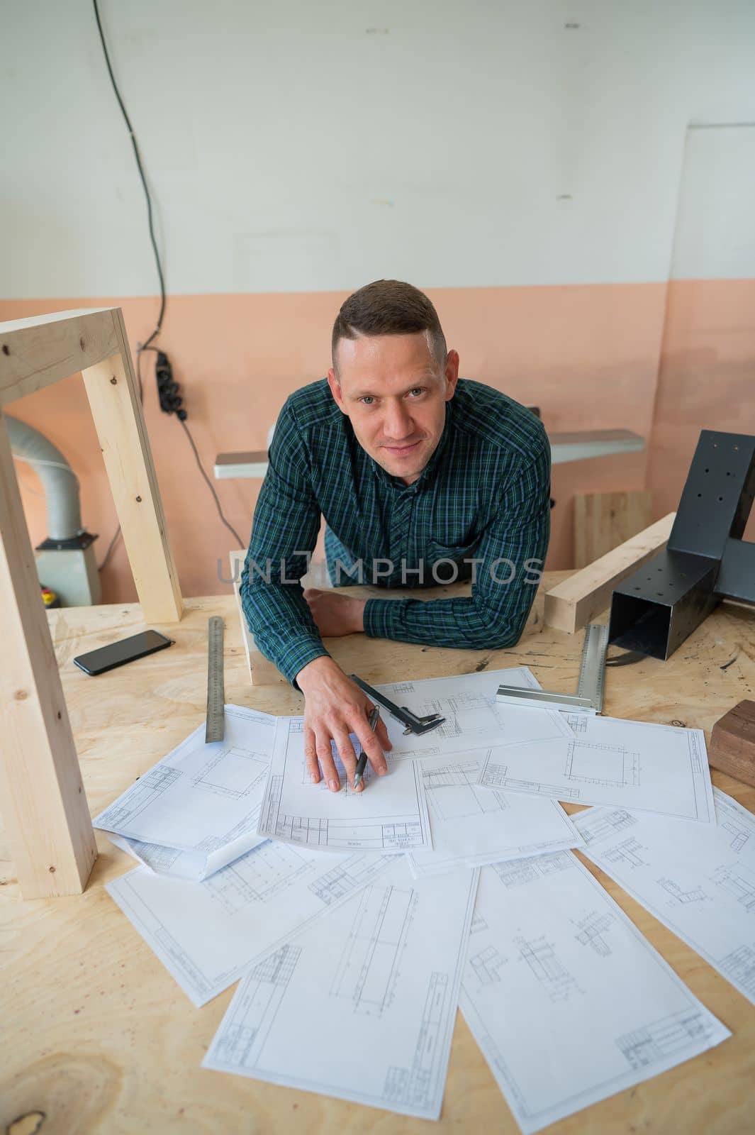 Portrait of a carpenter in a plaid shirt draws a workshop blueprint