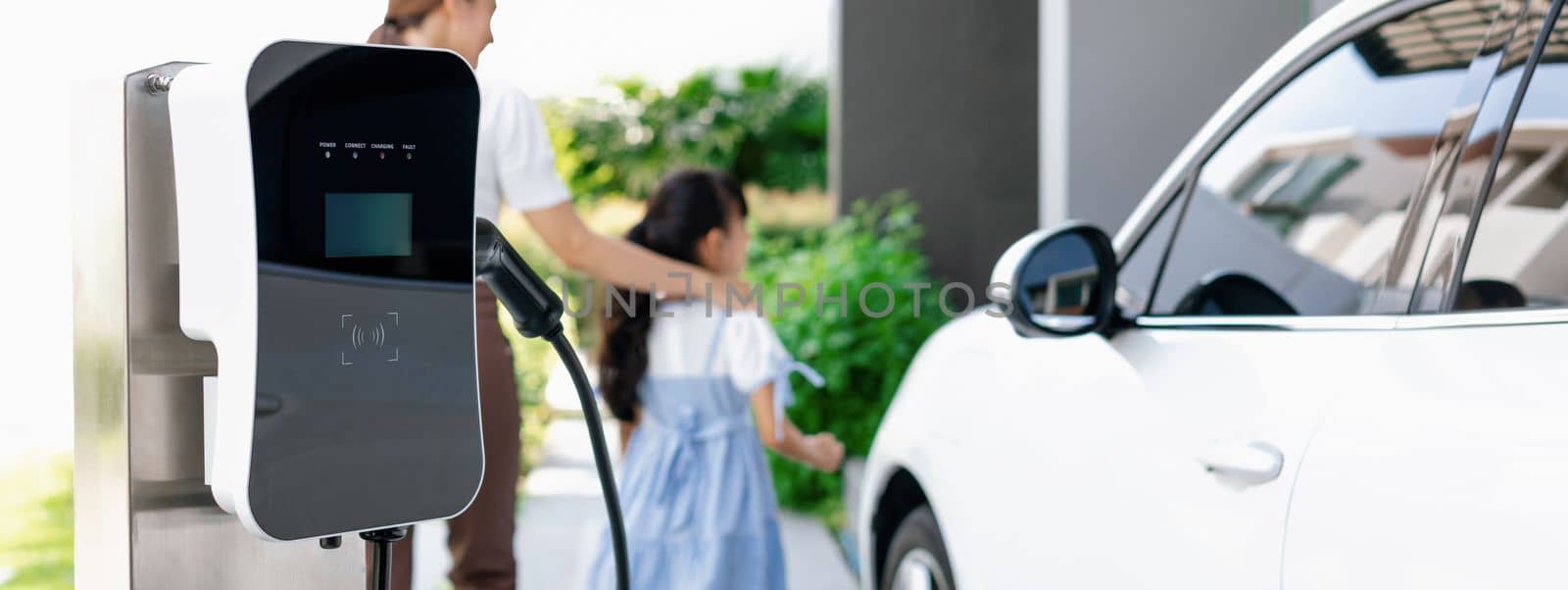 Focus progressive home EV charging point with blur woman and girl in background. by biancoblue