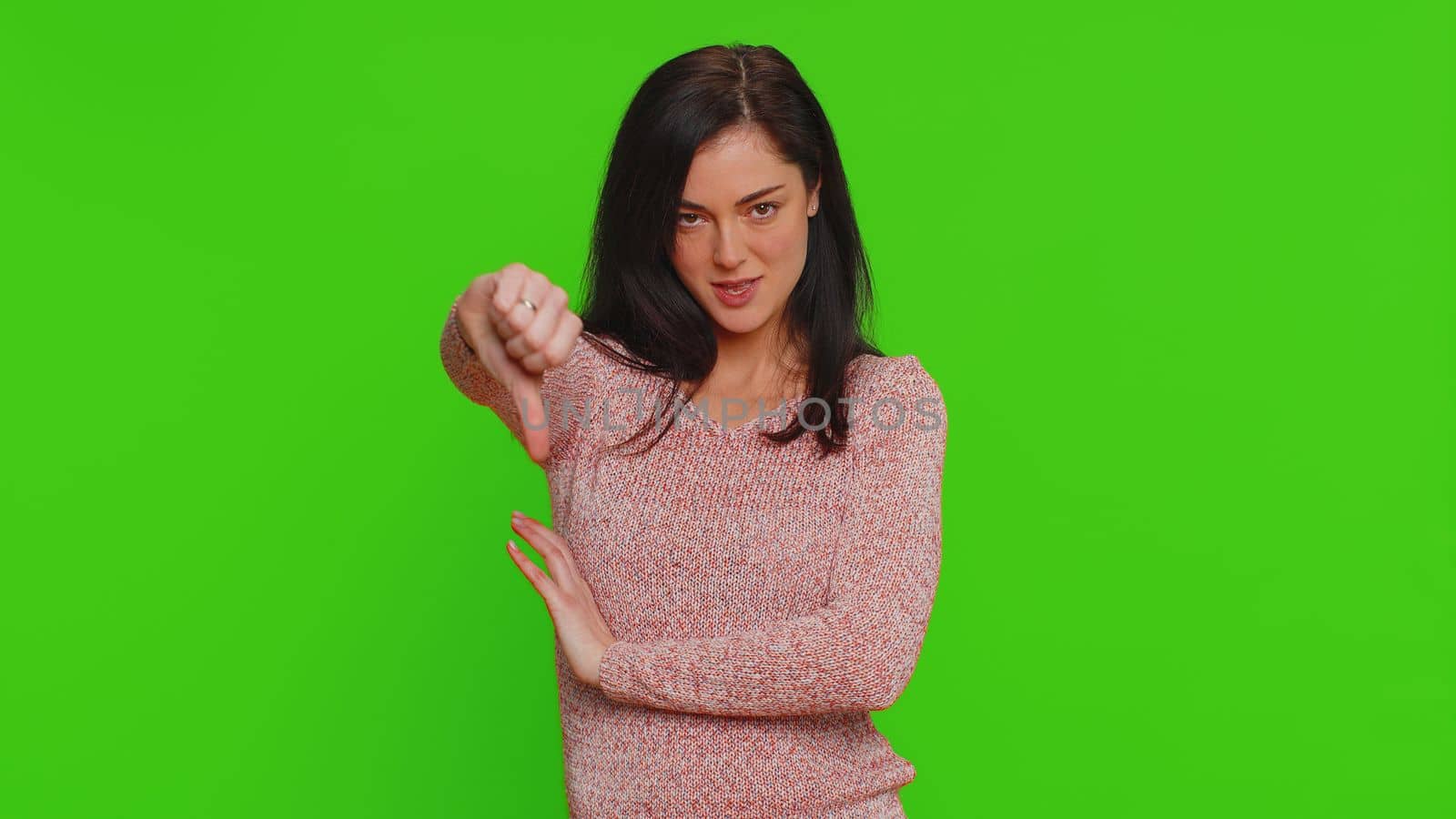 Dislike. Upset unhappy pretty woman in sweater showing thumbs down sign gesture, expressing discontent, disapproval, dissatisfied dislike. Young adult girl. Indoor studio shot on chroma key background