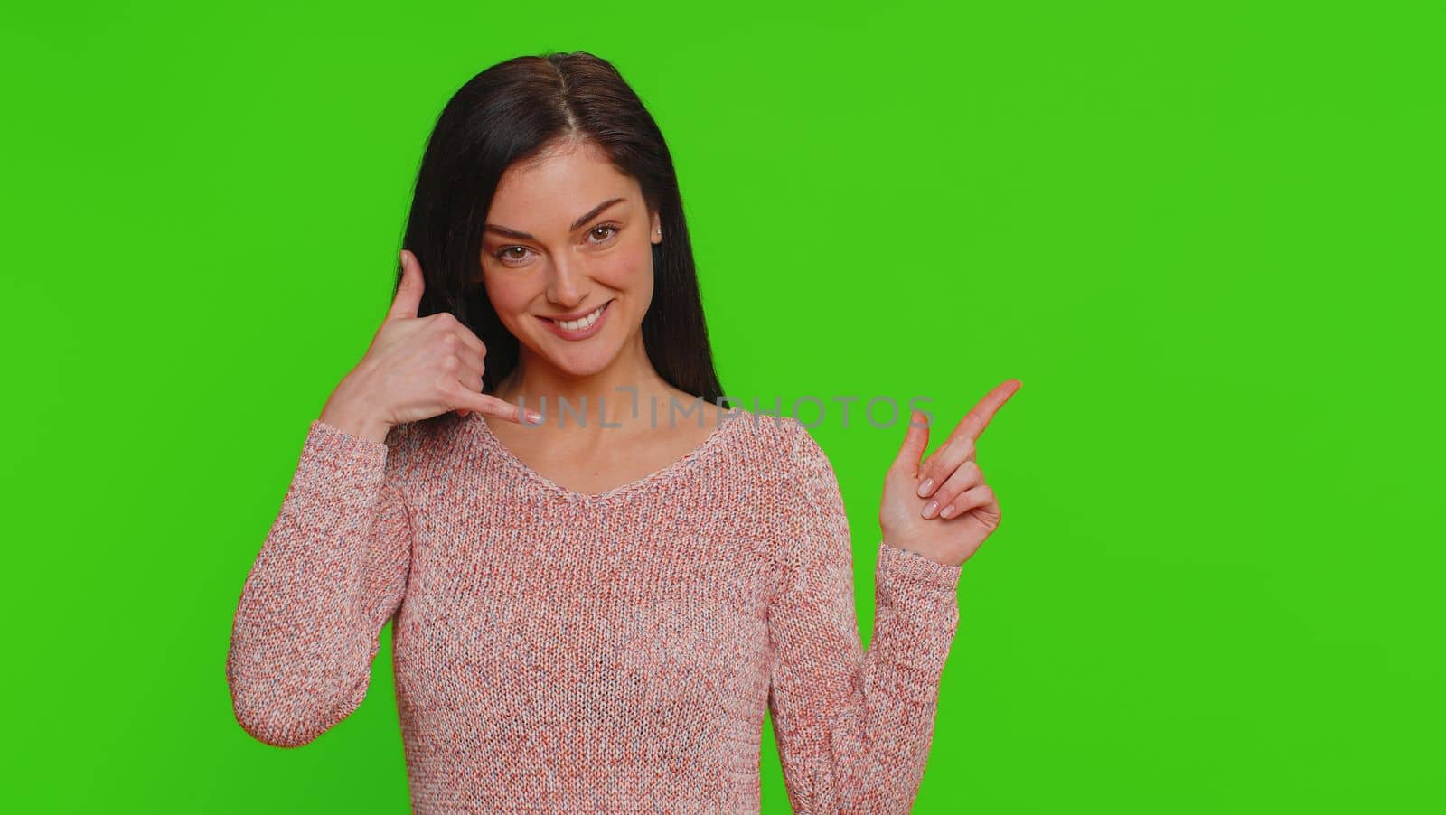 Call us, here is contact number. Young woman looking at camera doing phone gesture like says hey you call me back, conversation. Girl showing advertising area isolated on green chroma key background