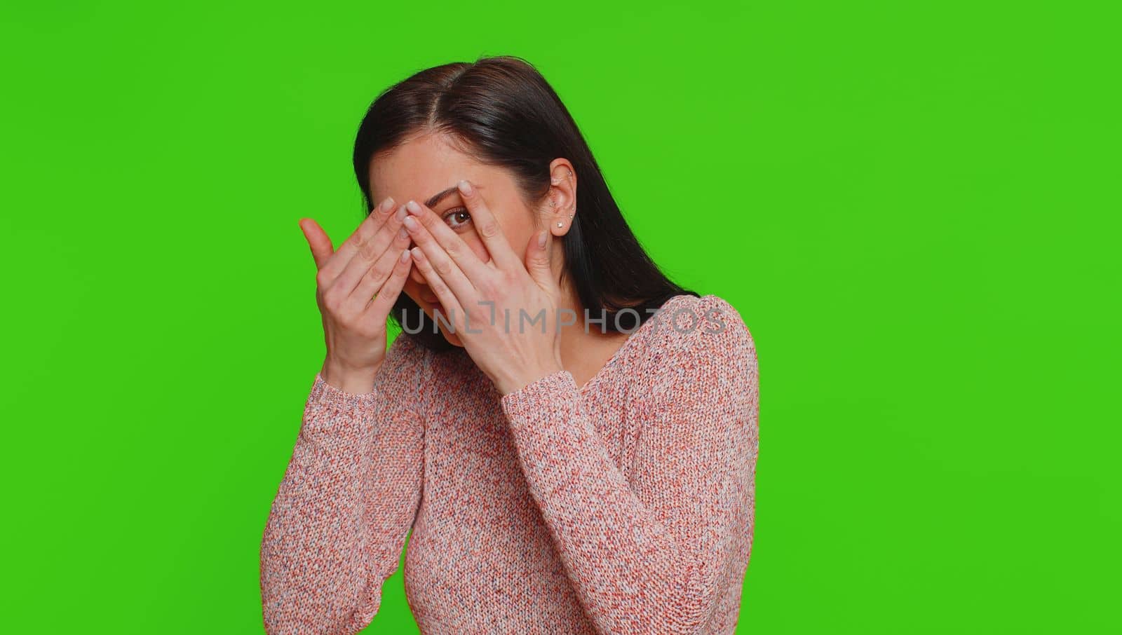 Nosy curious young woman closing eyes with hand and spying through fingers, hiding and peeping, binocular gesture, exploring way, seeking something in distance. Girl isolated on chroma key background