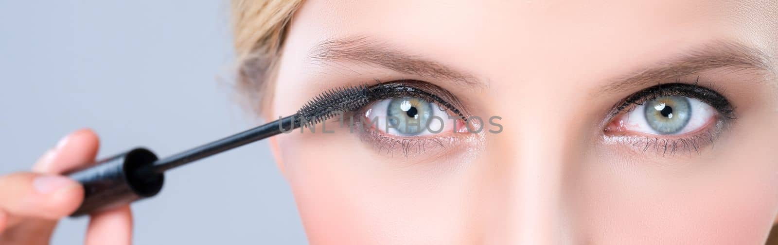 Closeup beautiful woman putting alluring black mascara on long thick eyelashes. by biancoblue
