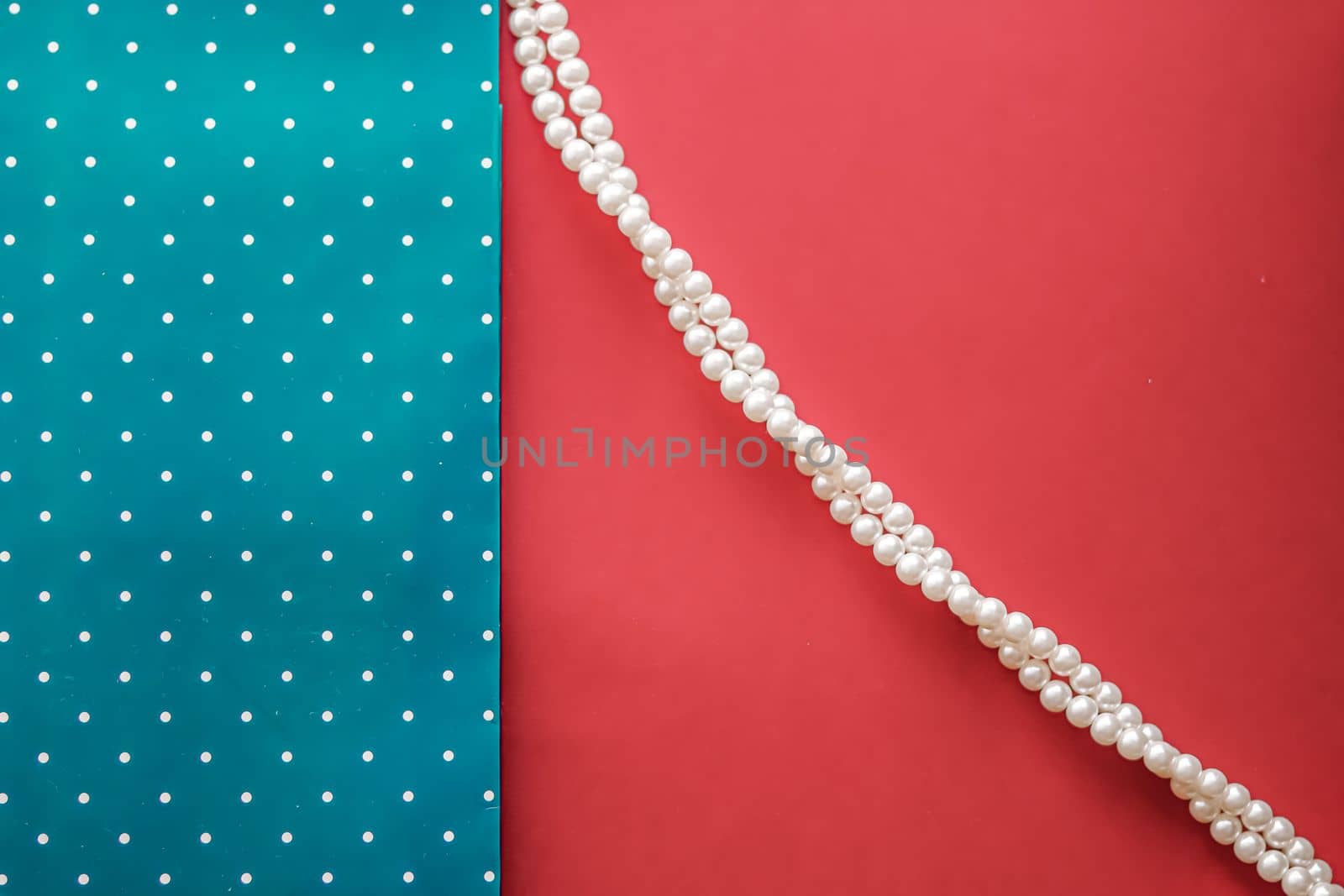 Pearl jewellery necklace and abstract blue polka dot background on coral backdrop.