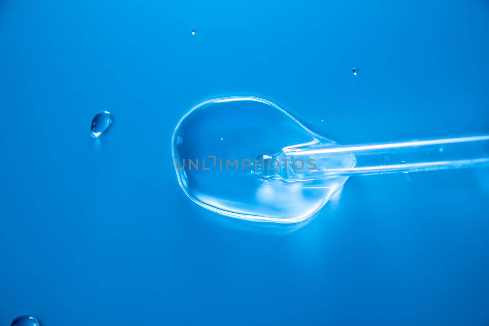 Water bubbles with cosmetic liquid drops of serum on a blue background of a laboratory glass pipette. Close-up of a pipette with drops.