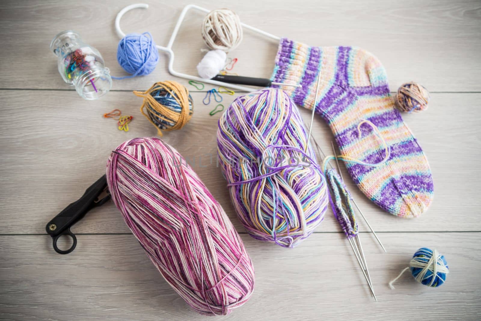 Colored threads, knitting needles and other items for hand knitting, on a light wooden table .