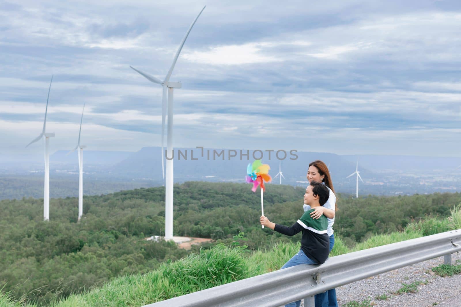 A progressive mother and her son are on vacation, enjoying the natural beauty of a lake at the bottom of a hill while the boy carries a toy windmill.