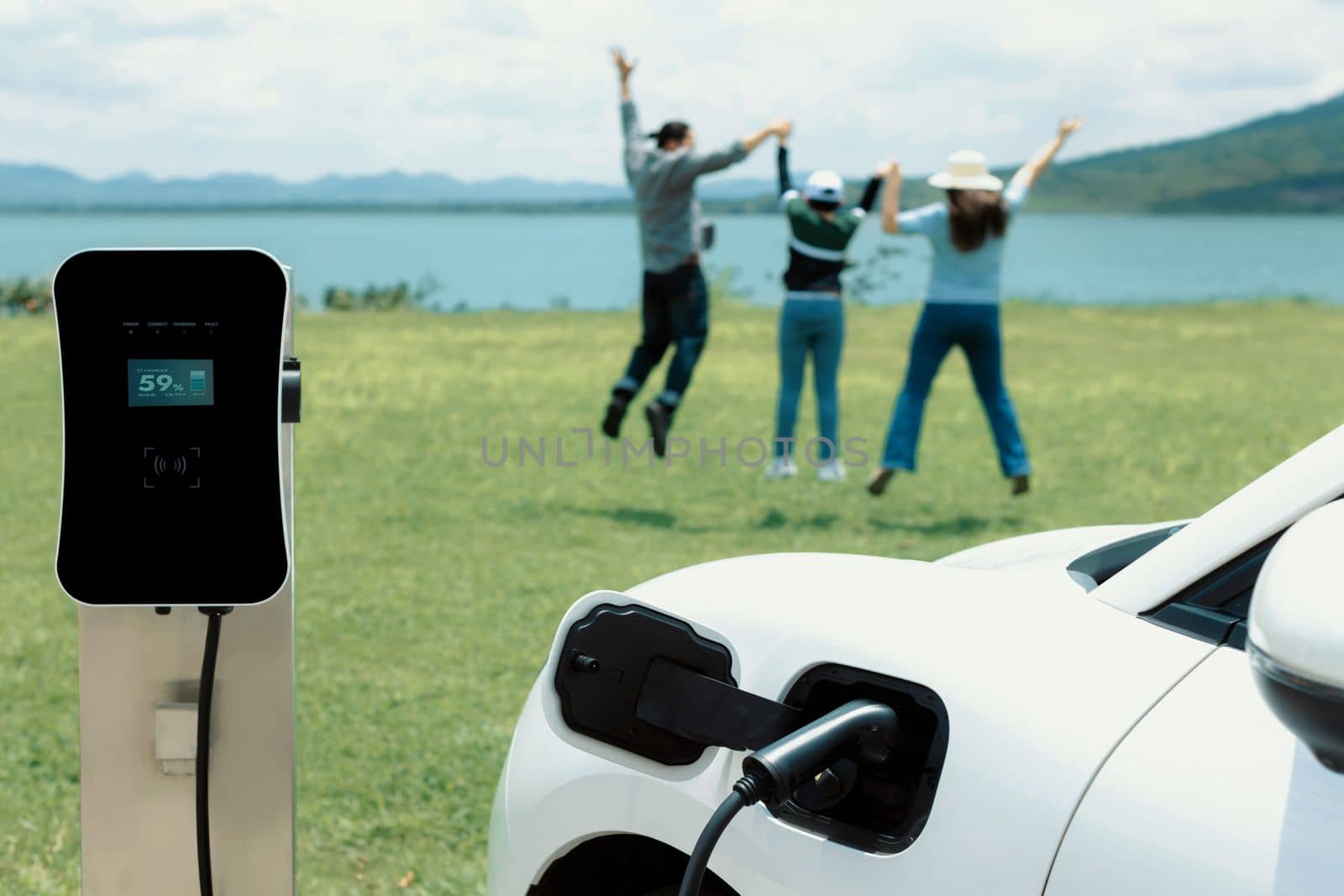 Concept of progressive happy family enjoying their time at green field and lake with electric vehicle. Electric vehicle driven by clean renewable from eco-friendly power sauce.