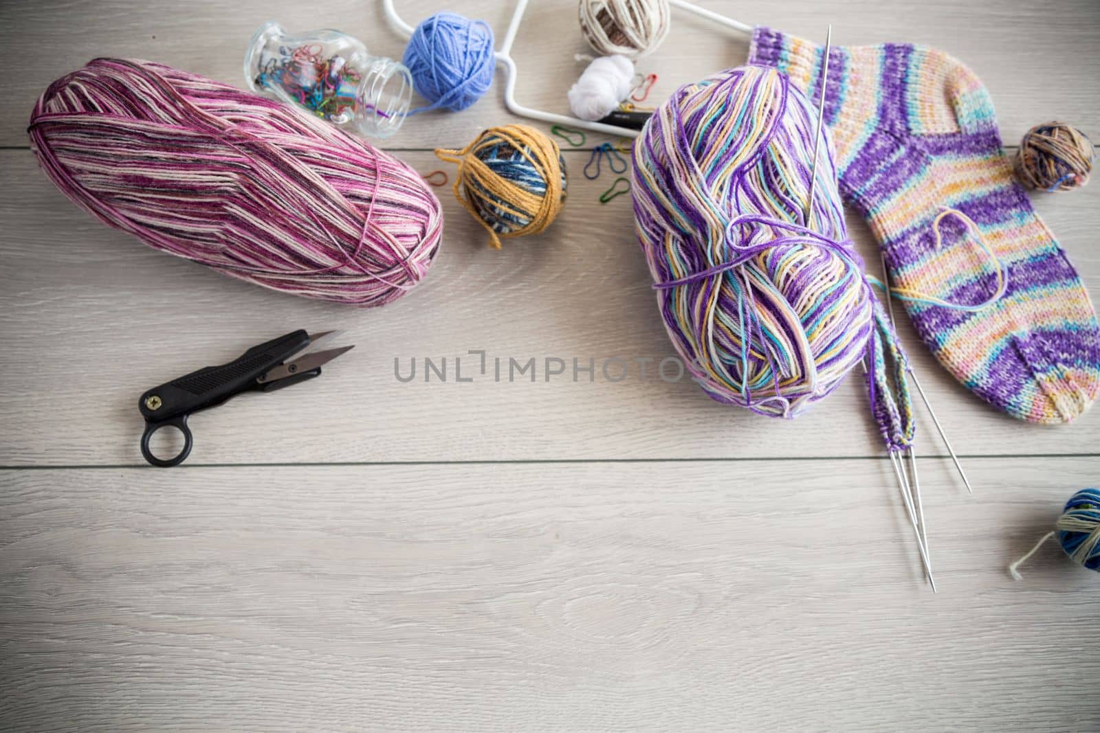 Colored threads, knitting needles and other items for hand knitting, on a light wooden table .