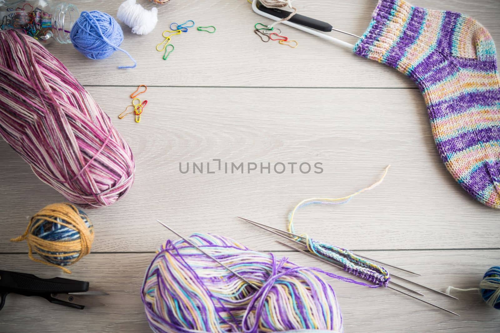 Colored threads, knitting needles and other items for hand knitting, on a light wooden table .