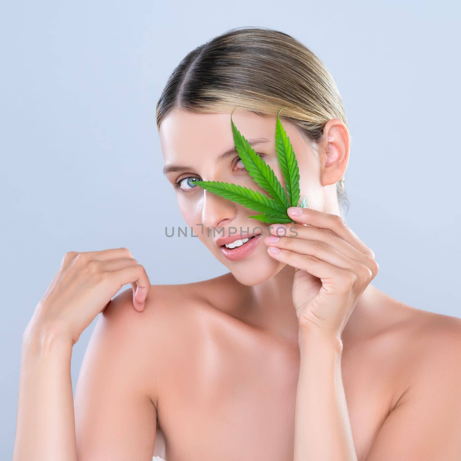 Alluring beautiful woman model portrait holding green leaf as concept for cannabis skincare cosmetic product for skin freshness treatment in isolated background.