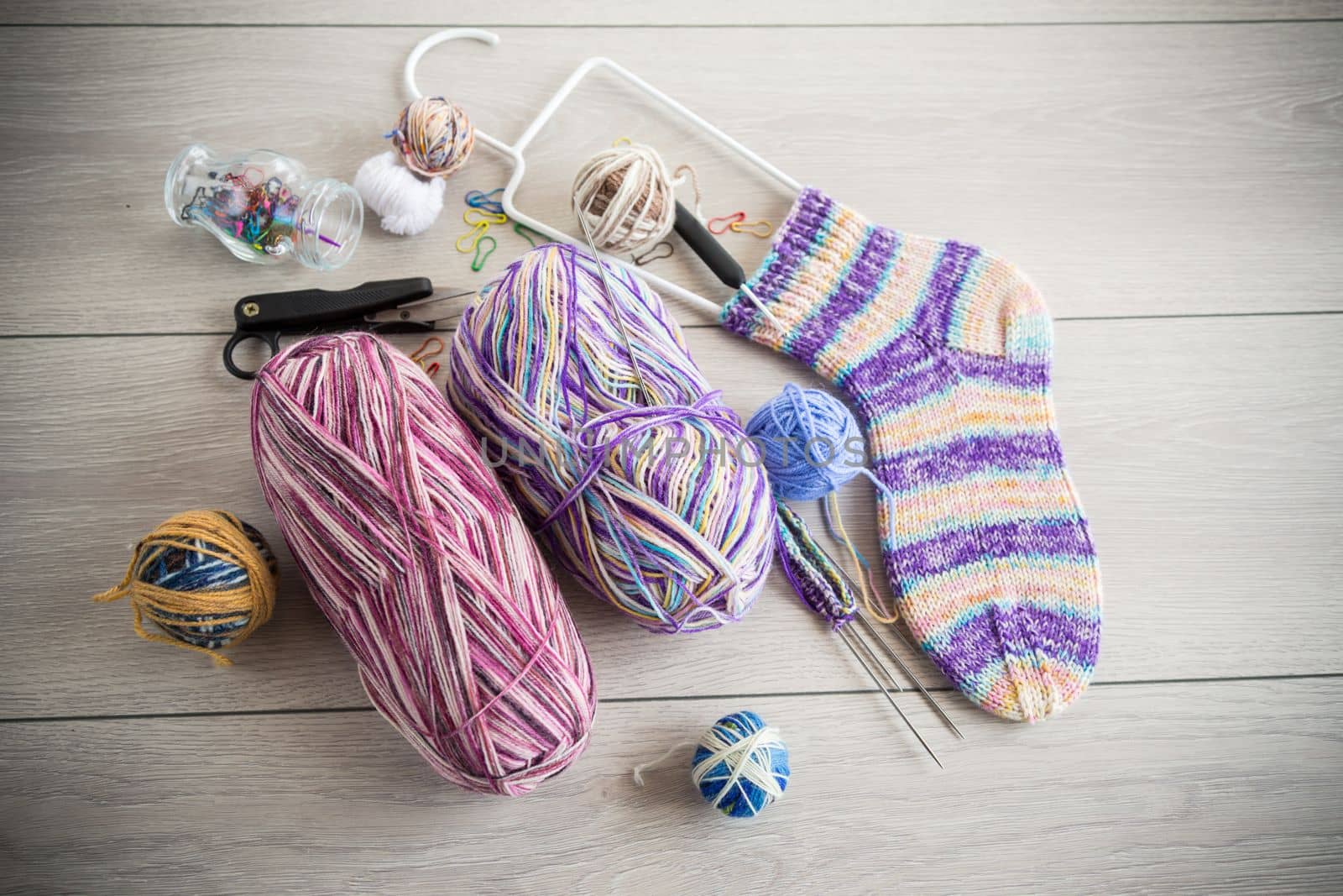 Colored threads, knitting needles and other items for hand knitting, on a light wooden table .