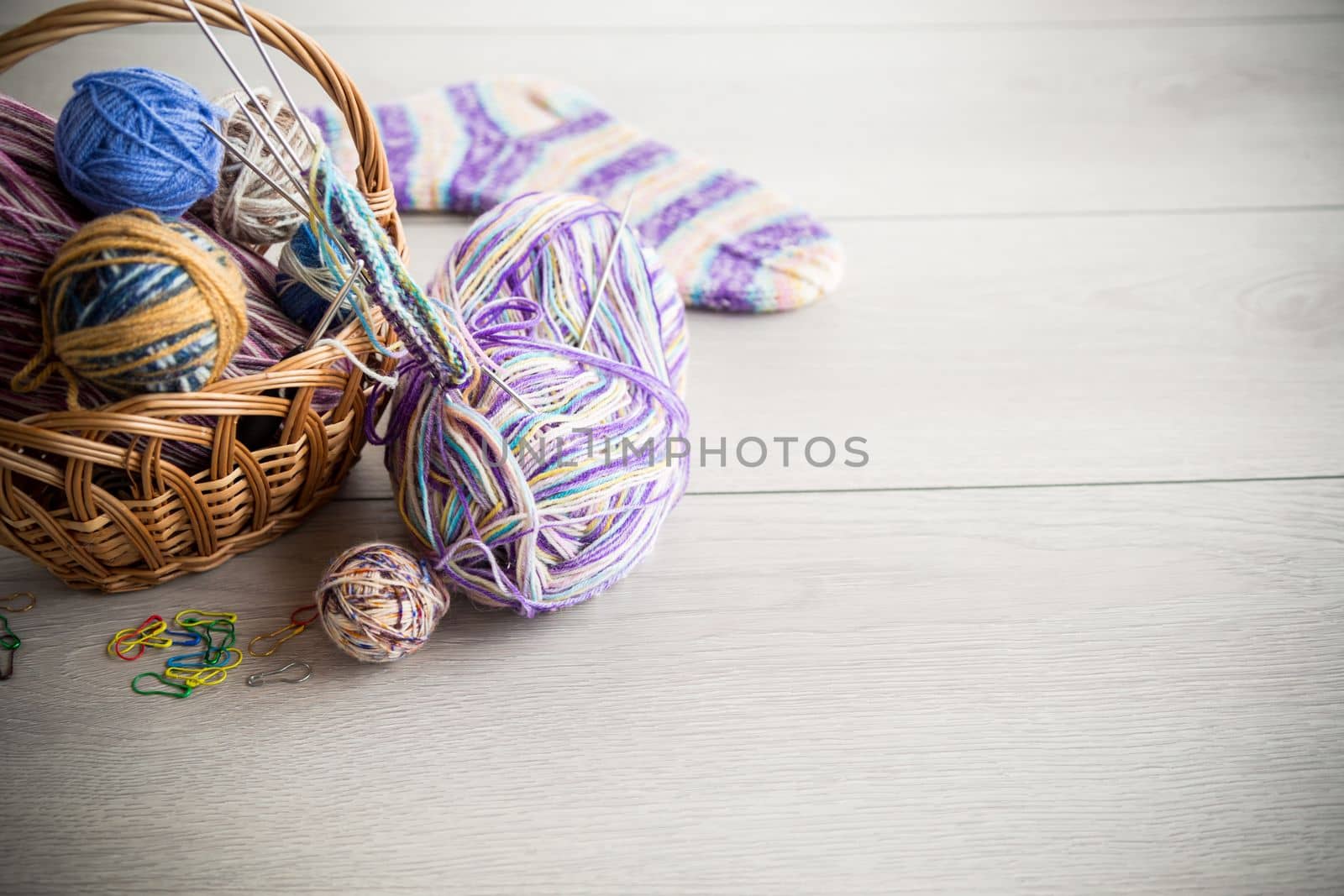 Colored threads, knitting needles and other items for hand knitting, on a light wooden table .