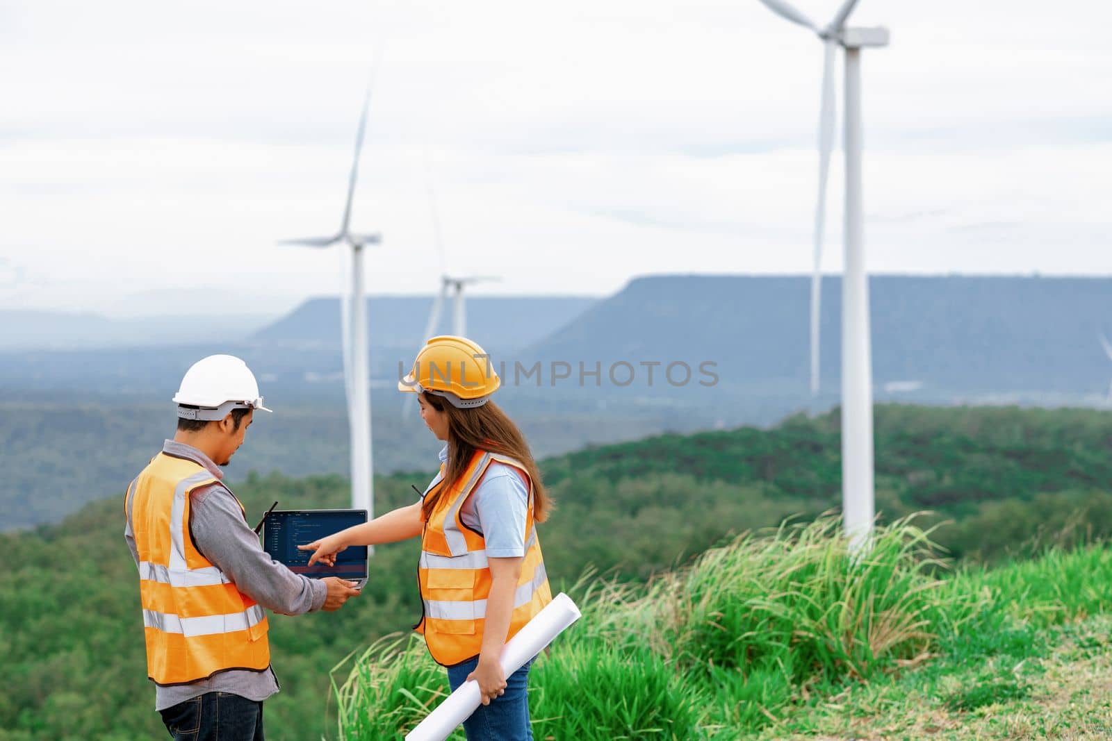 Male and female engineers working on a wind farm atop a hill or mountain in the rural. Progressive ideal for the future production of renewable, sustainable energy.