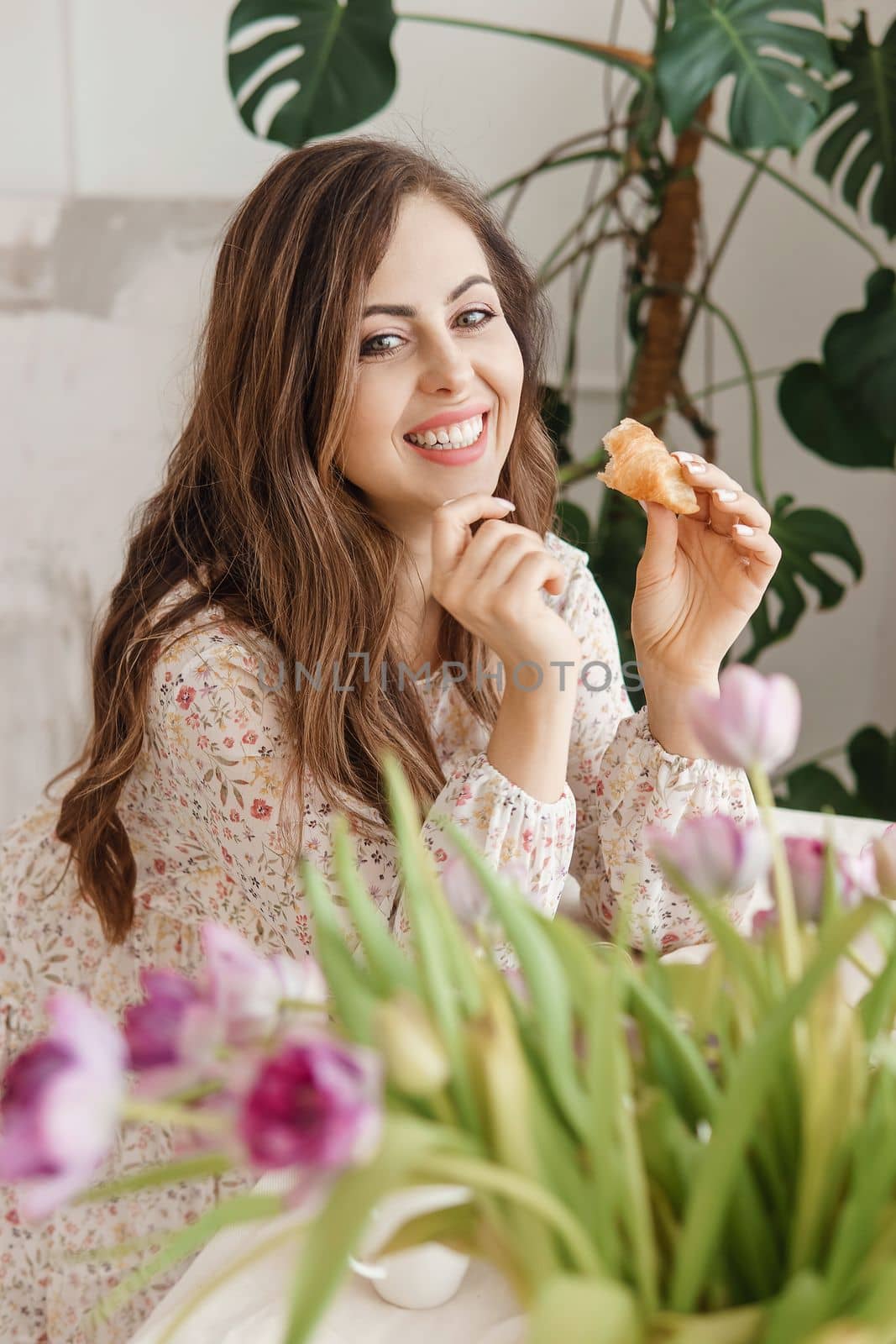 A brown-haired woman with long hair is having breakfast at the table with croissants and a cup of coffee. Spring portrait