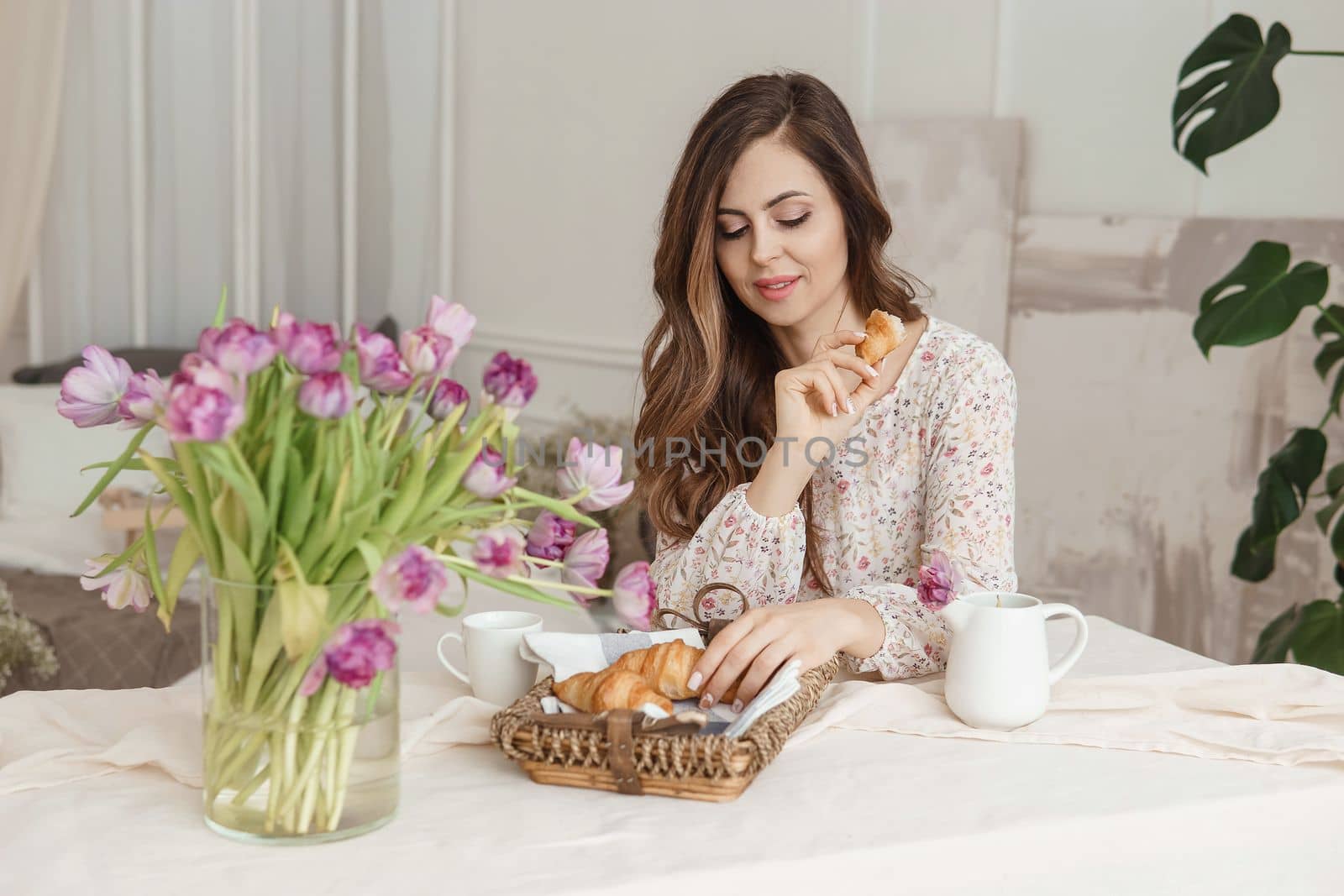 A brown-haired woman with long hair is having breakfast at the table with croissants and a cup of coffee. Spring portrait