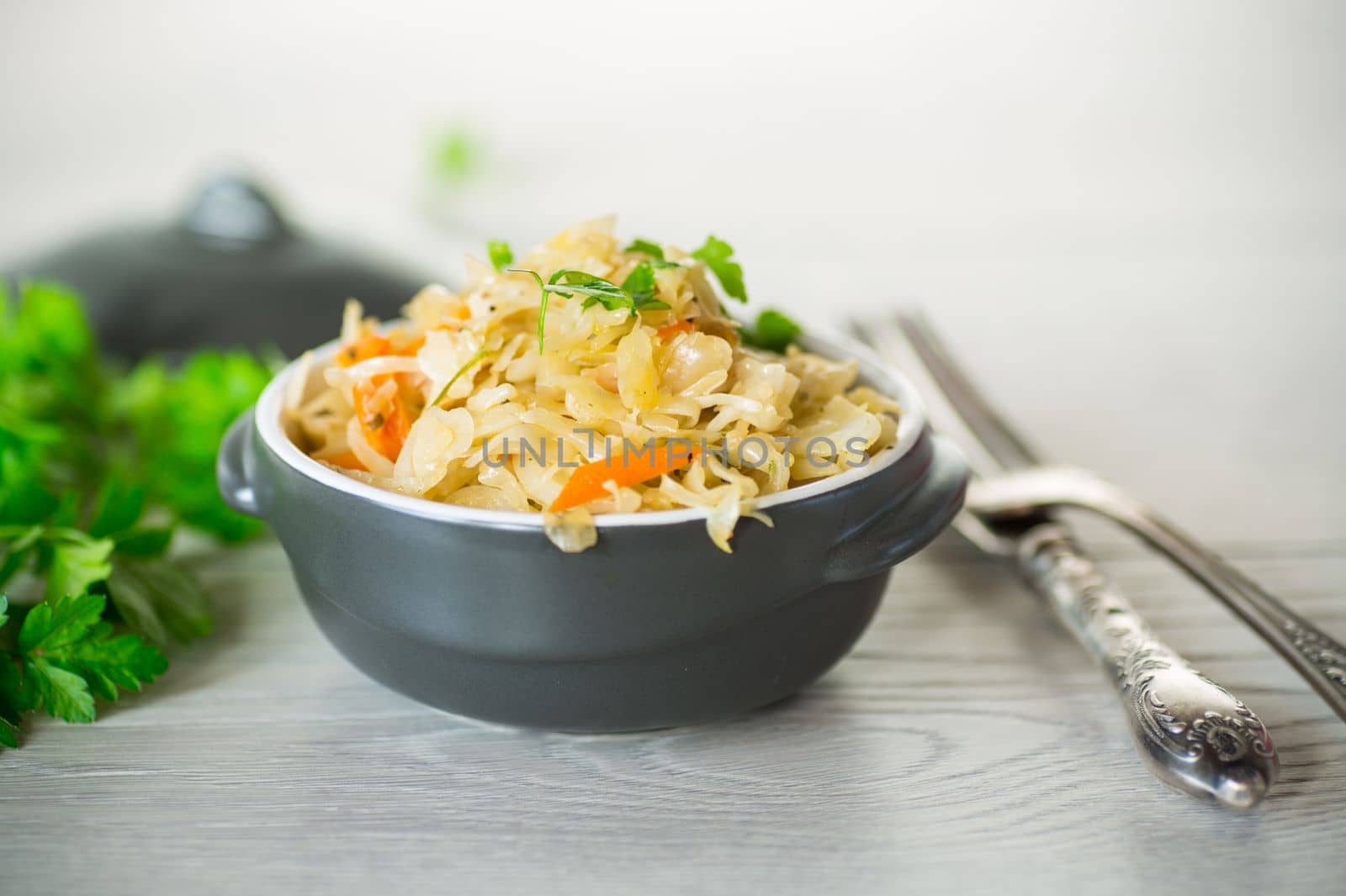 Braised cabbage with carrots, onions and herbs in a ceramic bowl on a wooden table.