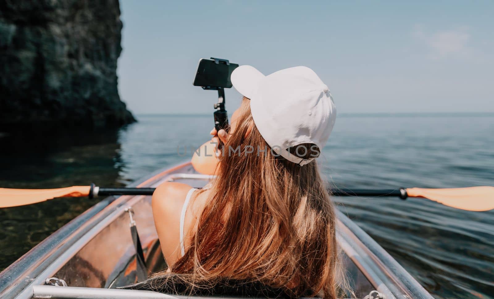 Woman in kayak back view. Happy young woman with long hair floating in transparent kayak on the crystal clear sea. Summer holiday vacation and cheerful female people having fun on the boat.