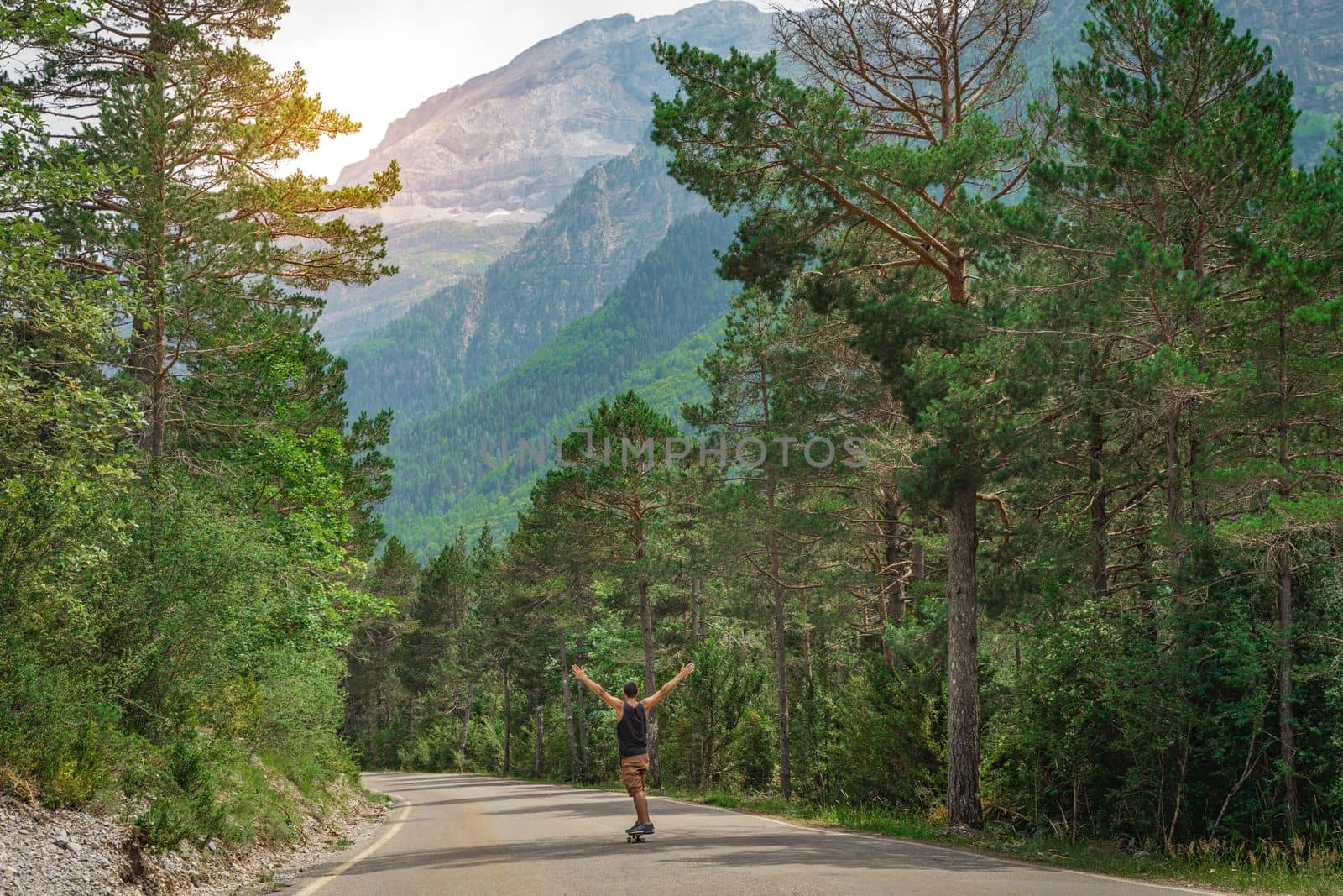 Hipster guy with long board with open arms enjoying life in the middle of a mountain road and a beautiful landscape. High quality photo