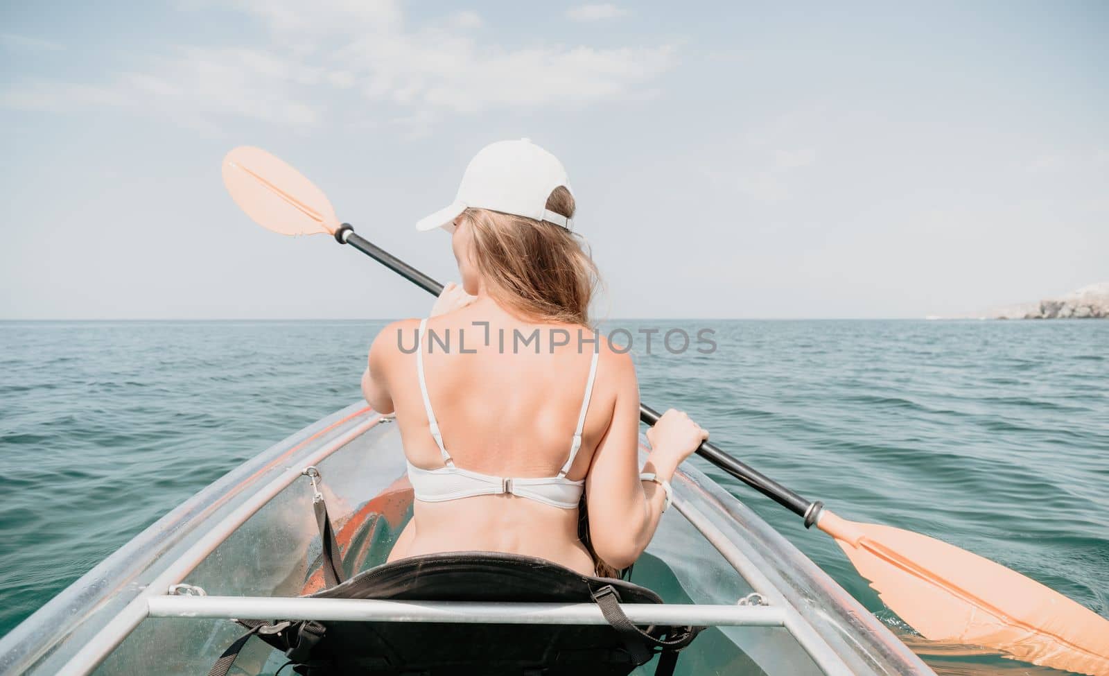 Woman in kayak back view. Happy young woman with long hair floating in transparent kayak on the crystal clear sea. Summer holiday vacation and cheerful female people having fun on the boat.