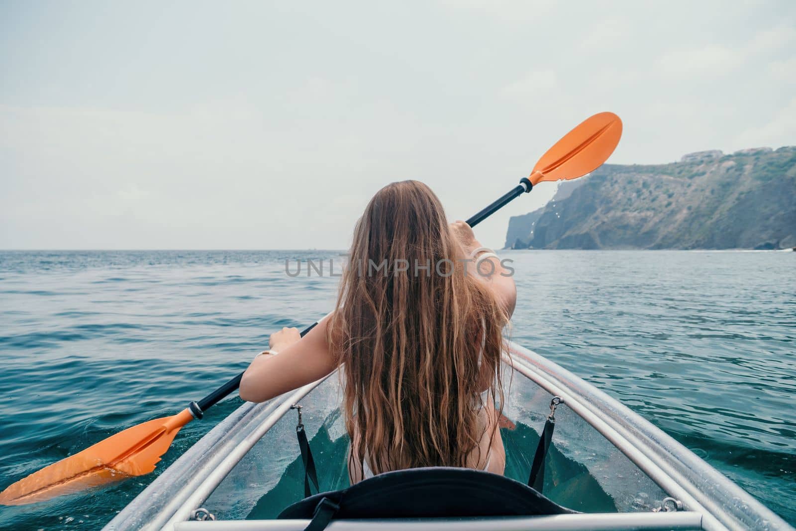 Woman in kayak back view. Happy young woman with long hair floating in transparent kayak on the crystal clear sea. Summer holiday vacation and cheerful female people relaxing having fun on the boat by panophotograph