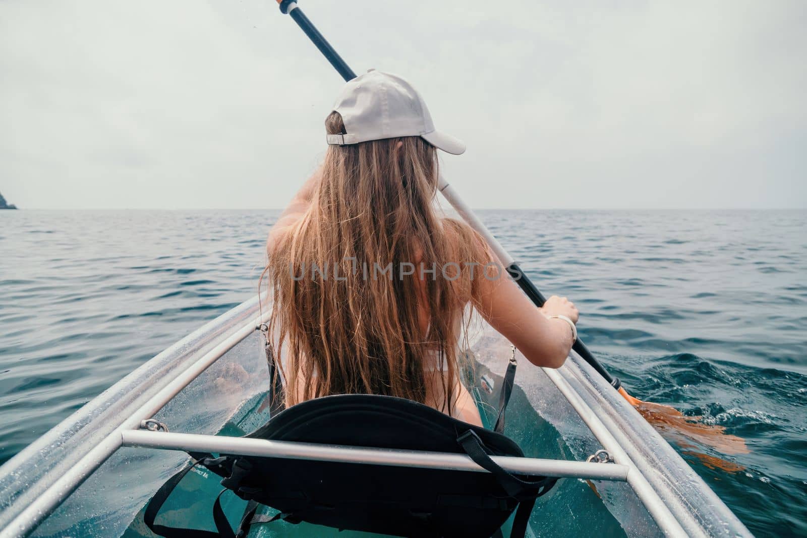 Woman in kayak back view. Happy young woman with long hair floating in transparent kayak on the crystal clear sea. Summer holiday vacation and cheerful female people having fun on the boat.