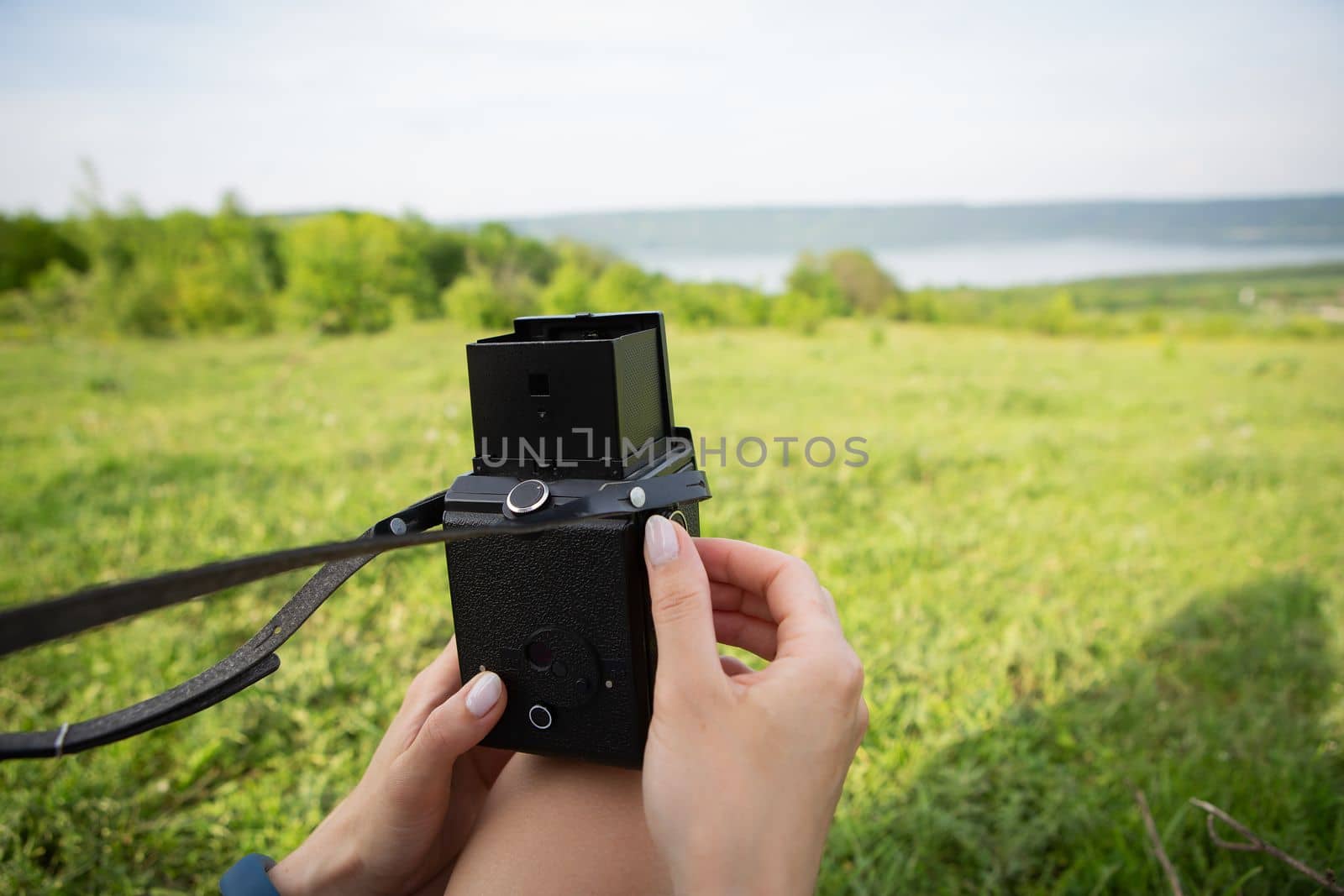 Photo of the hands of a young photographer with an old camera shooting a very beautiful landscape of a lake and a green meadow