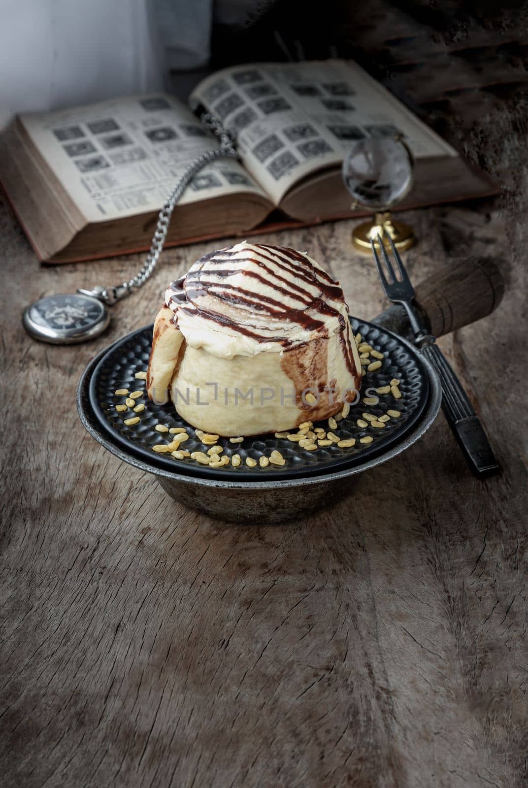 Cinnamon roll topped with rich cream cheese frosting served with Metal fork on old rustic wooden background. Homemade soft chocolate bun, The concept of delicious dessert, Space for text, Selective focus.
