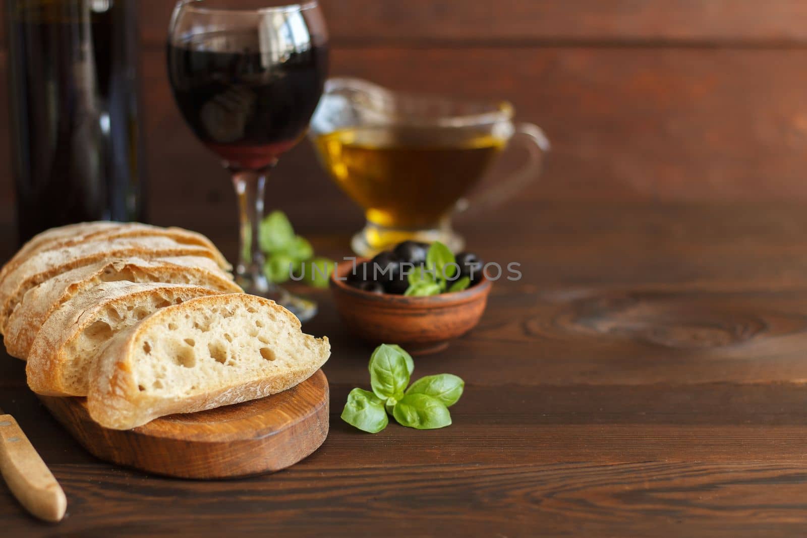 Sliced ciabatta with red wine, olive oil, olives and basil on a wooden background.