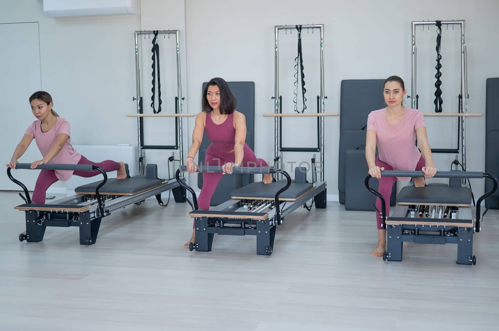 Three Asian women in pink sportswear do exercises on the reformer machine. Pilates classes. by mrwed54