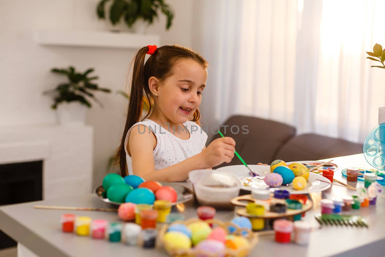 Cute little girl paints eggs with a brush. Easter concept
