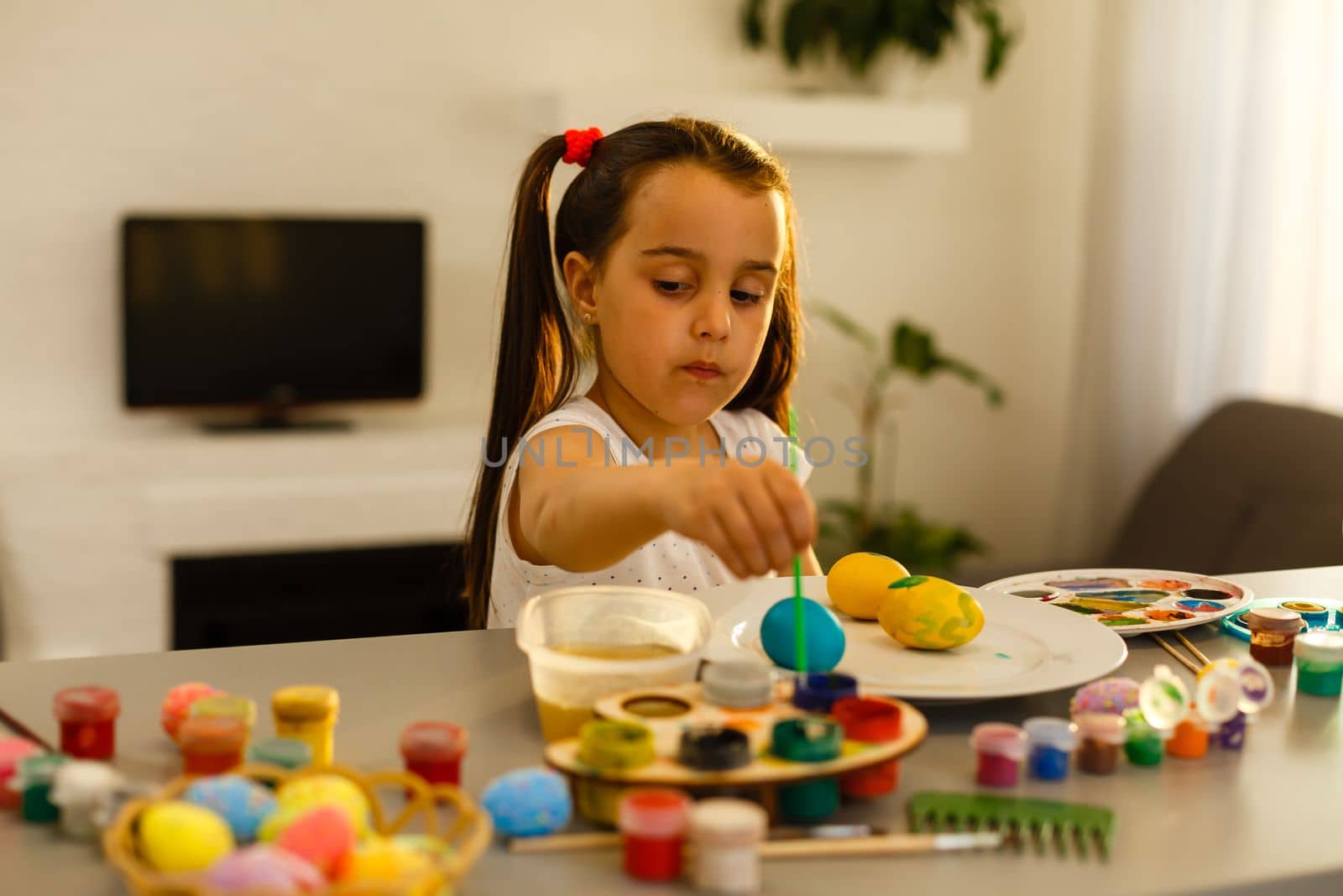 Cute little girl paints eggs with a brush. Easter concept