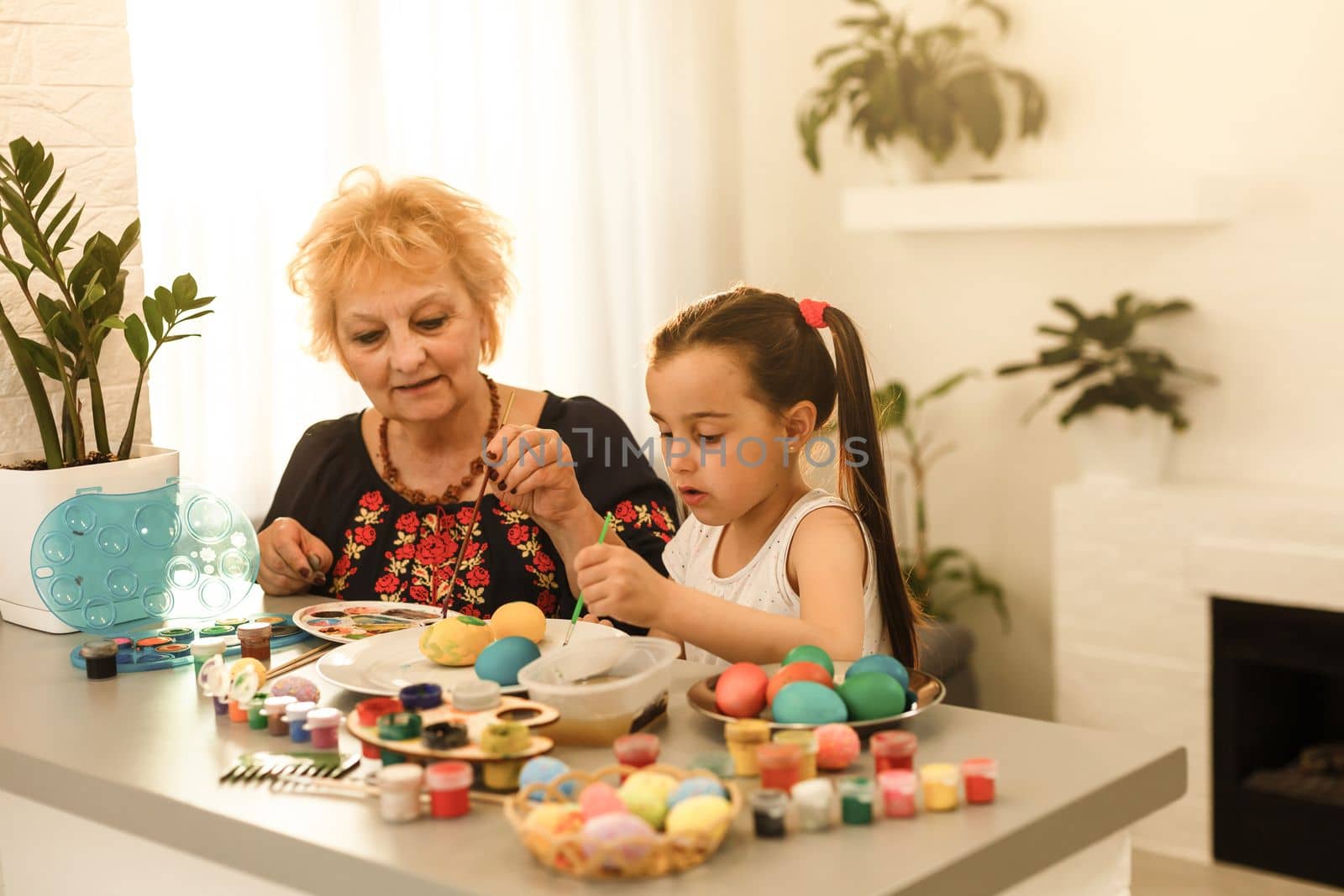 Young cheerful woman and her little daughter looking through painted Easter eggs and choosing one for grandmother