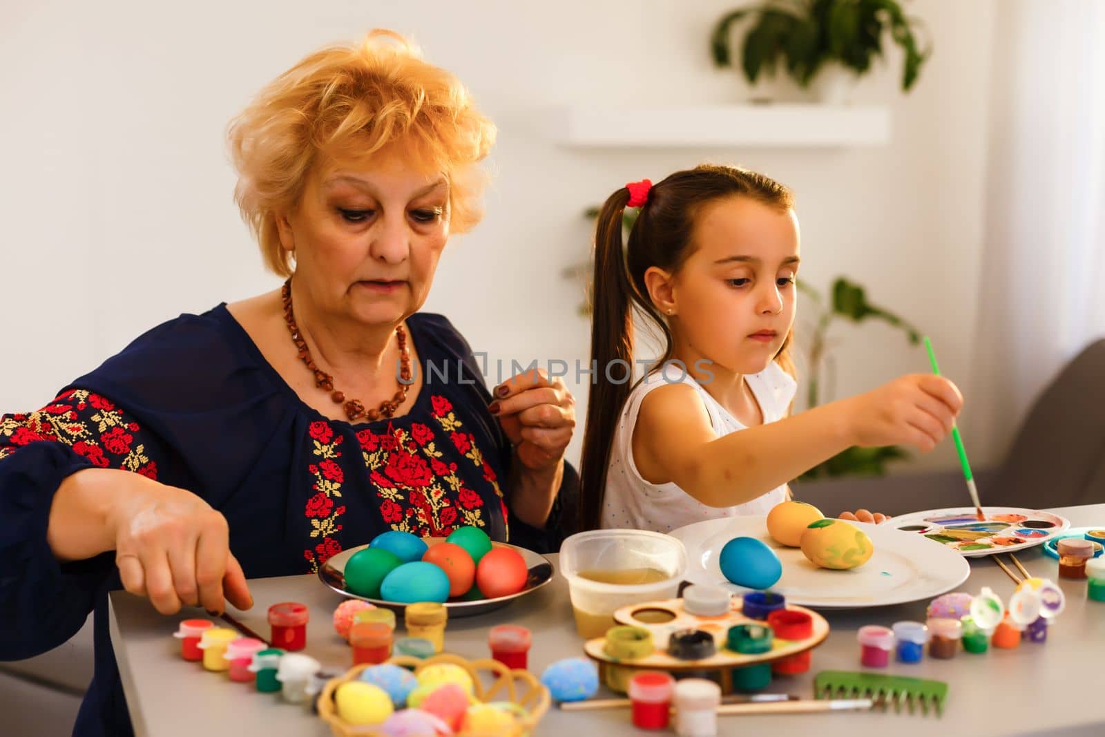 Grandmother with granddaughter are coloring eggs for Easter.