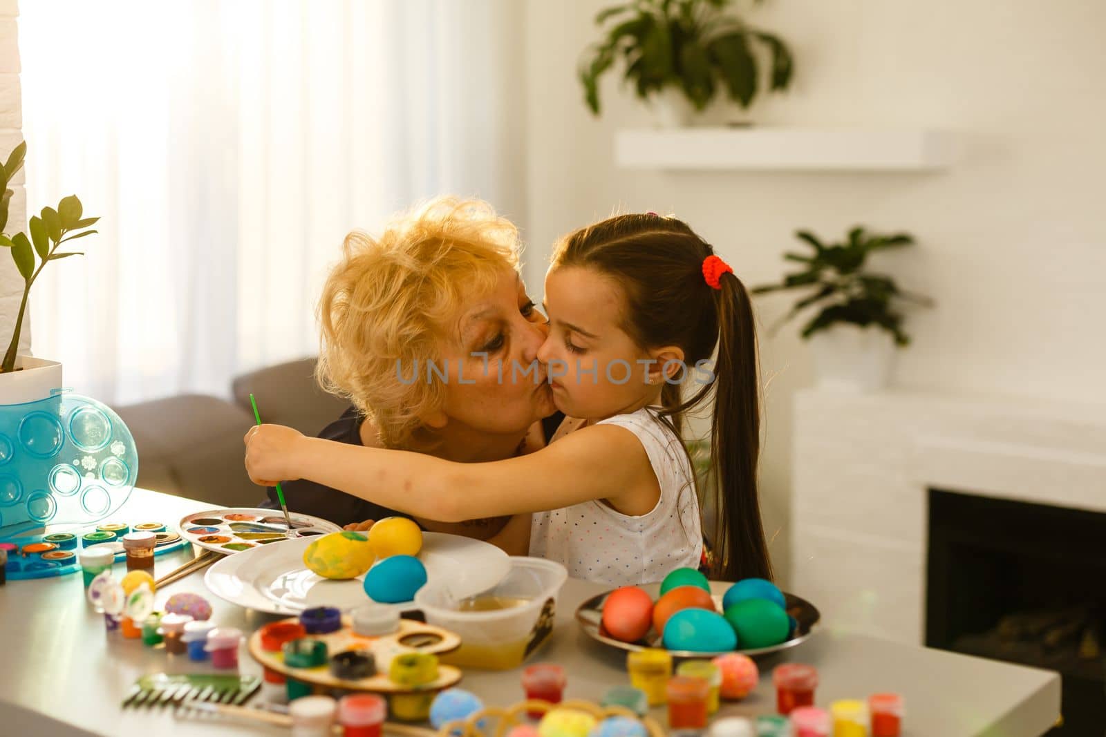 Little girl and her grandmother painting Easter eggs at home. by Andelov13