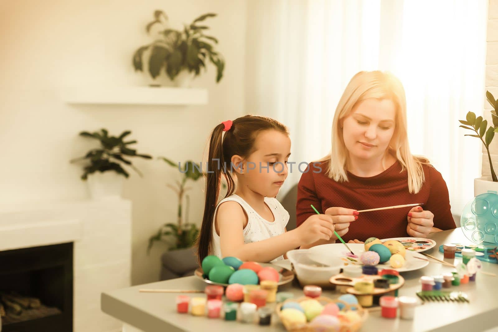 Happy easter! A mother and her daughter painting Easter eggs. Happy family preparing for Easter. Cute little child girl wearing bunny ears on Easter day by Andelov13