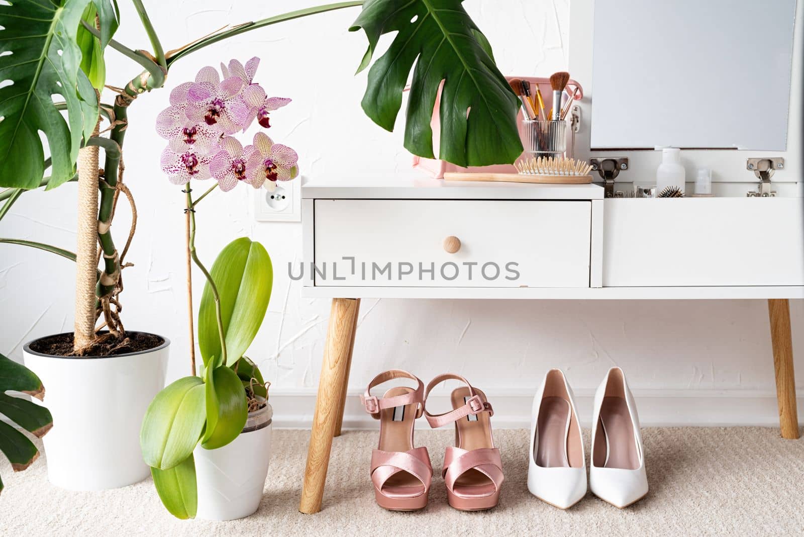 Stylish light room interior with elegant vanity table and monstera plants, beauty and fashion