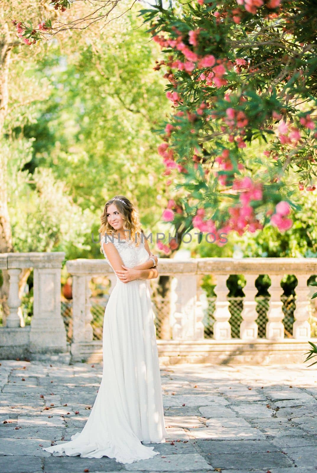 Smiling bride in a white dress stands under a flowering tree in the garden. High quality photo