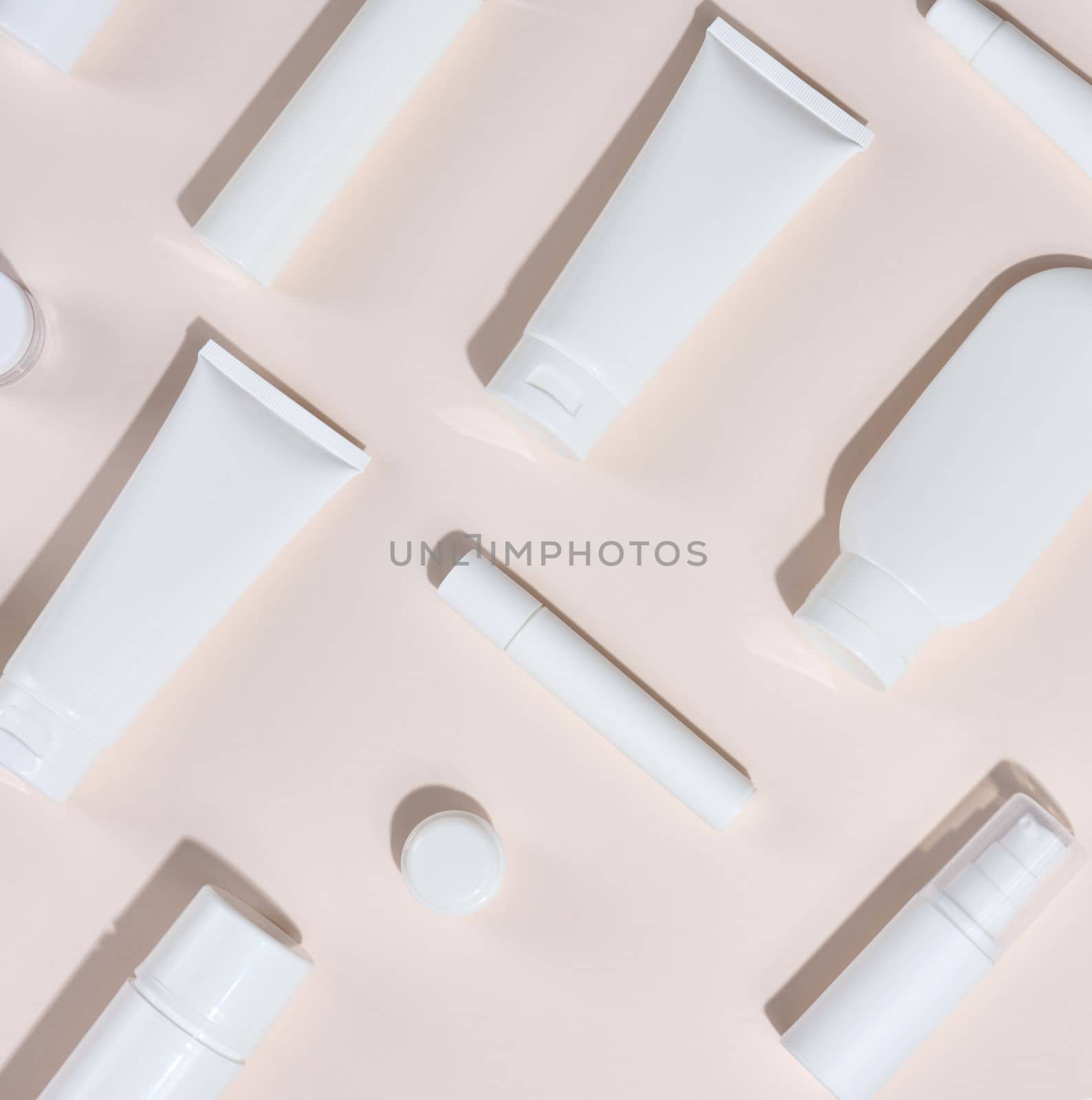 White plastic tubes, jars and other form of packaging for cosmetics on a beige background, top view.  by ndanko